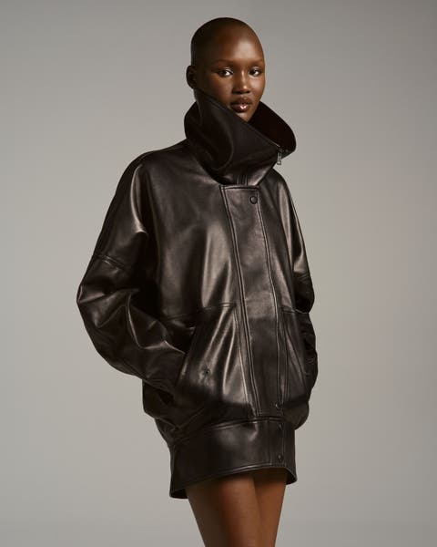 Model wearing an oversized dark leather jacket with dramatic gathered/shearling-trim collar