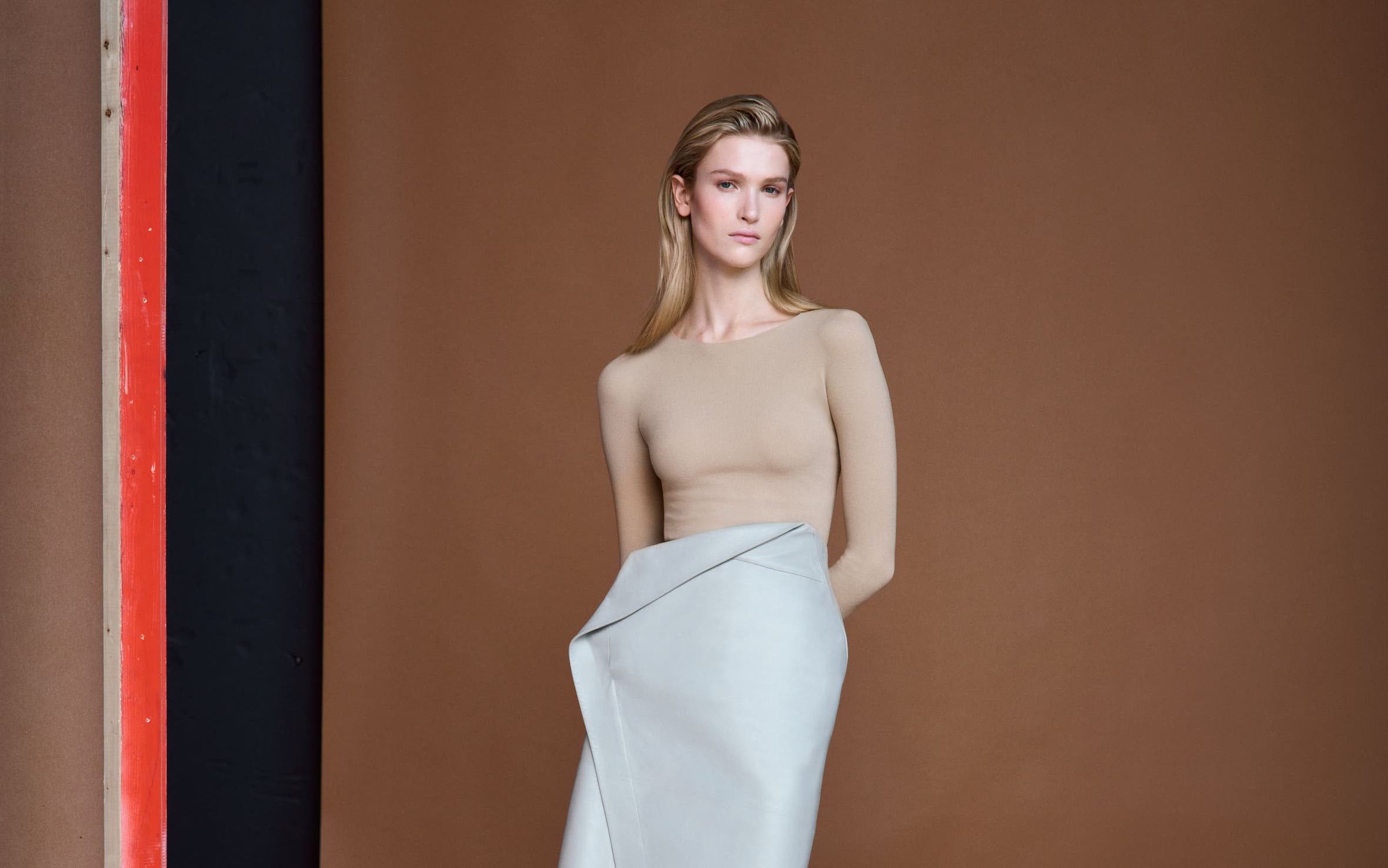 Woman wearing a beige long-sleeve top with a light blue-green wrap-style midi skirt and grey pointed-toe heels.