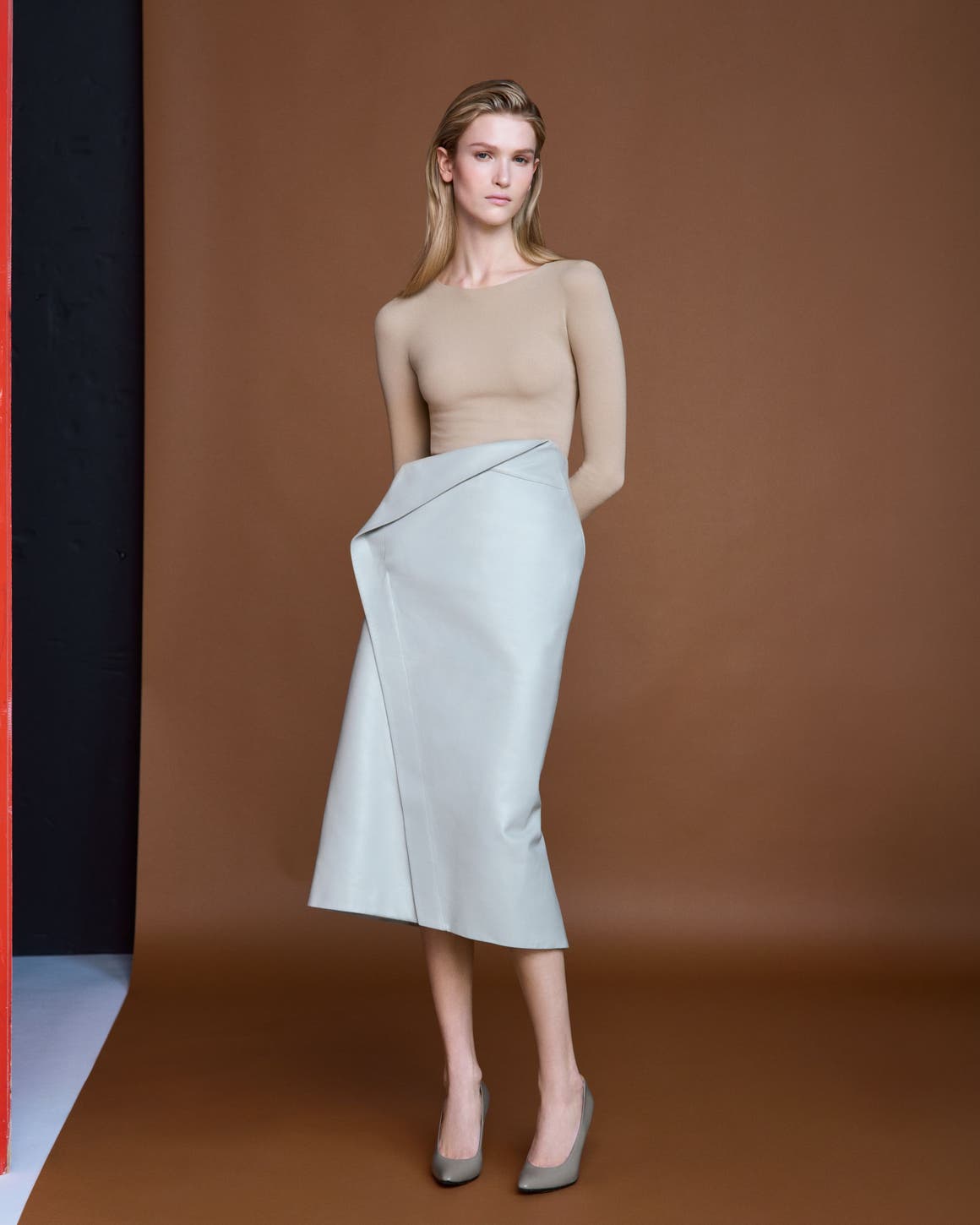 Woman wearing a beige long-sleeve top with a light blue-green wrap-style midi skirt and grey pointed-toe heels.
