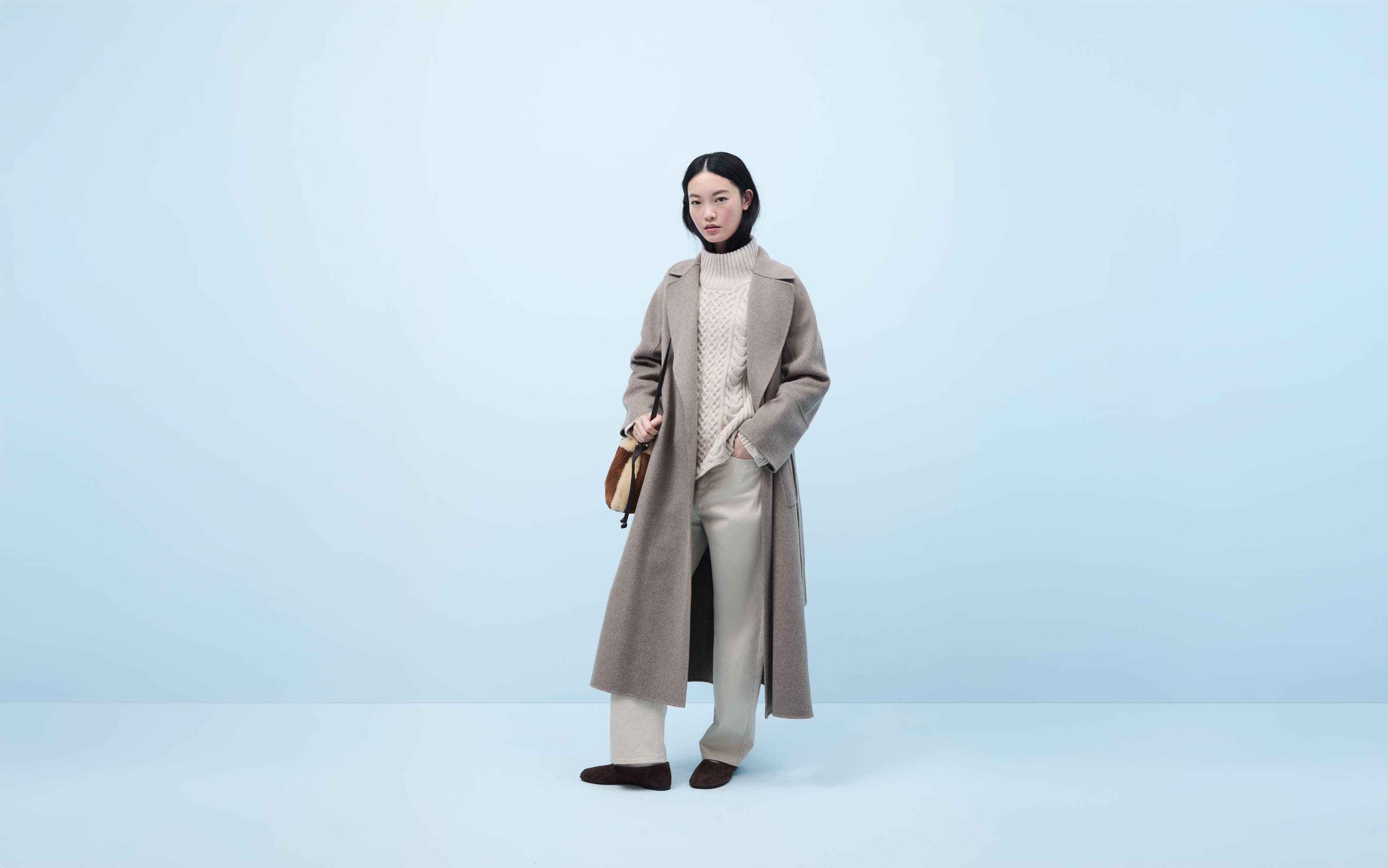 Woman wearing a coat, turtleneck sweater, pants, flats and a handbag.