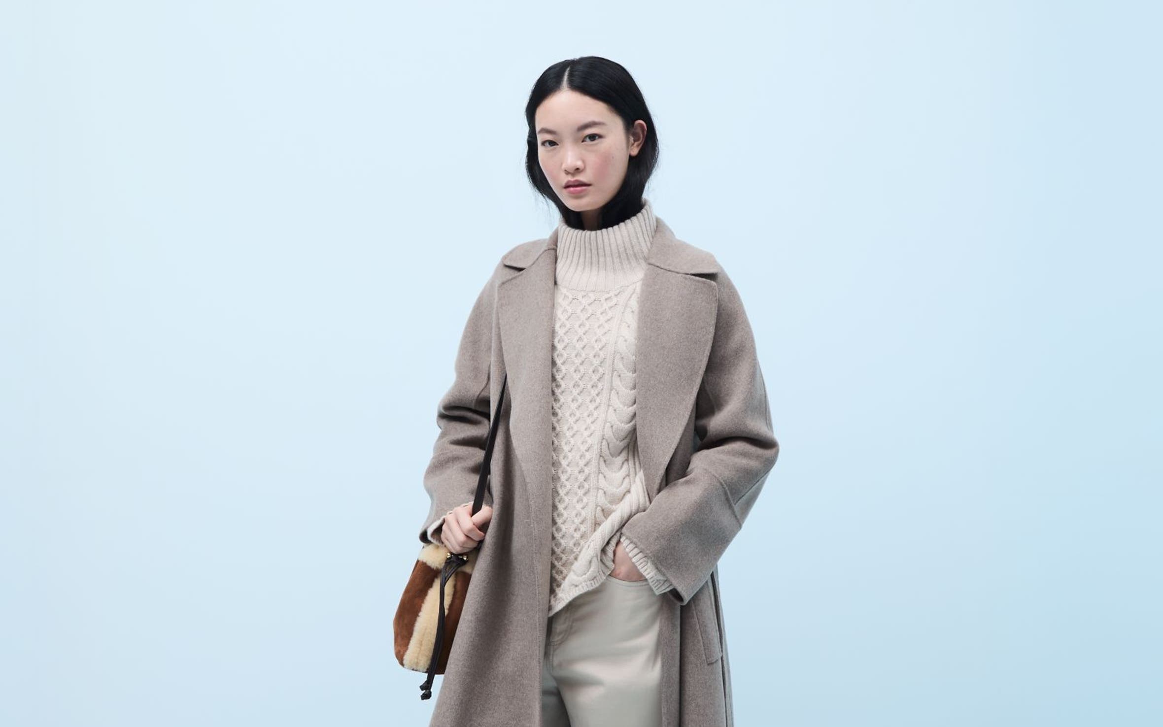 Woman wearing a coat, turtleneck sweater, pants, flats and a handbag.