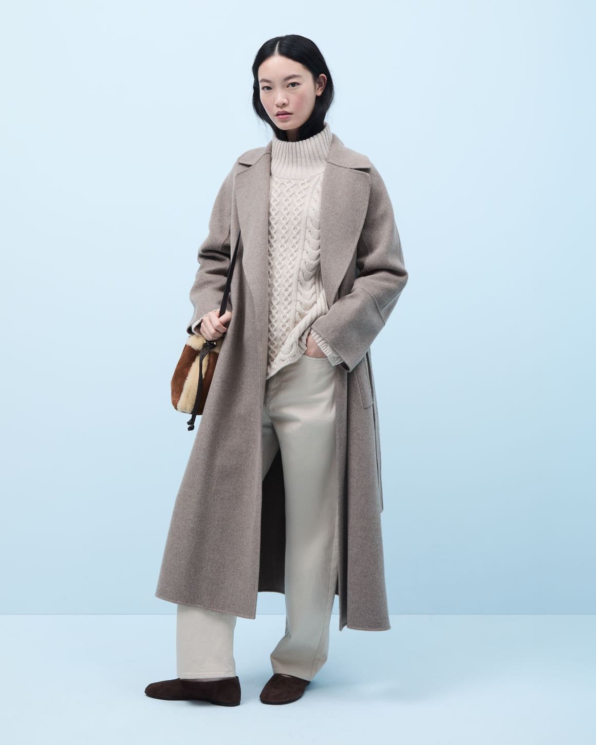 Woman wearing a coat, turtleneck sweater, pants, flats and a handbag.