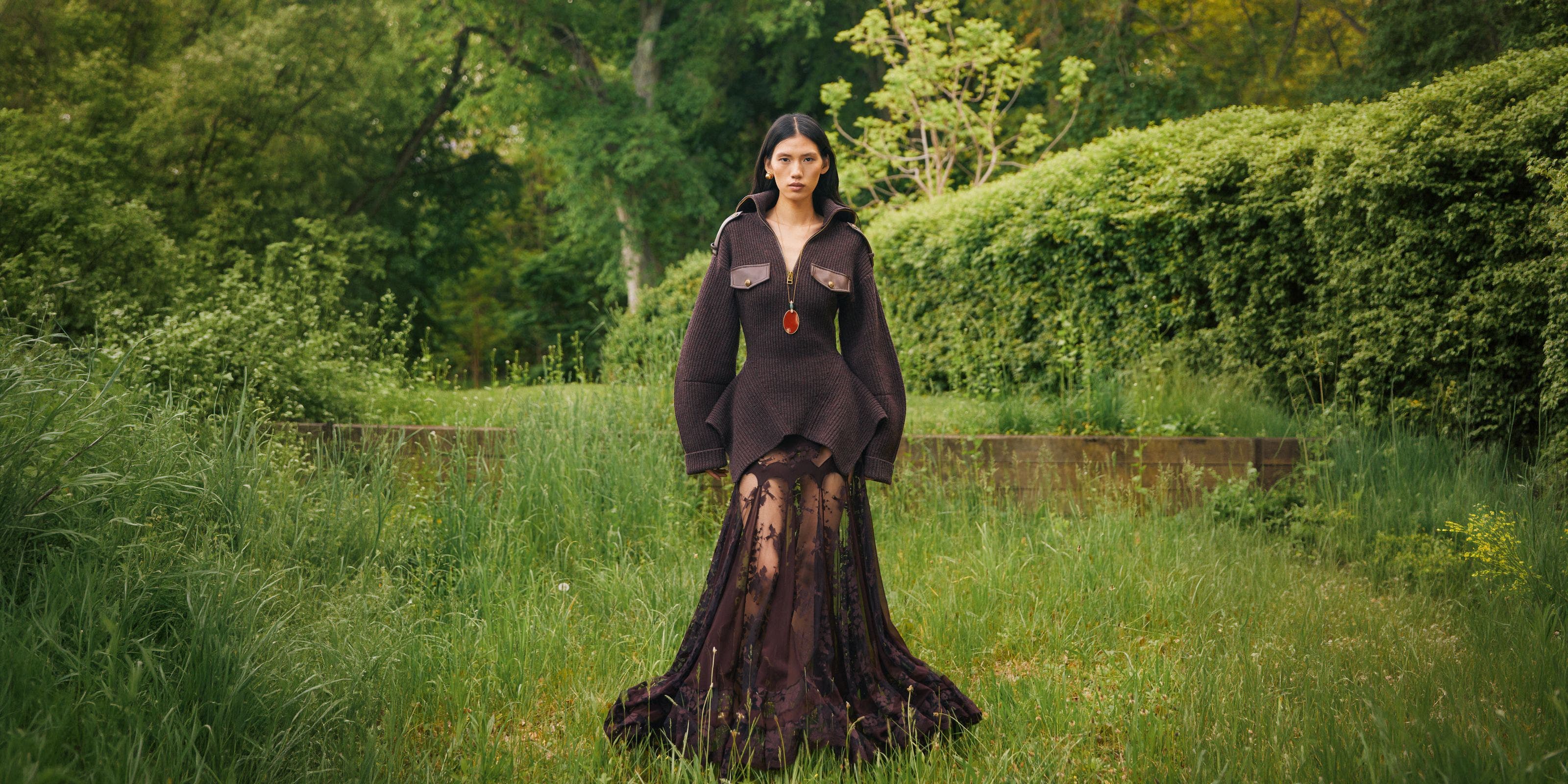 Woman wearing dark brown jacket with flowy gown.