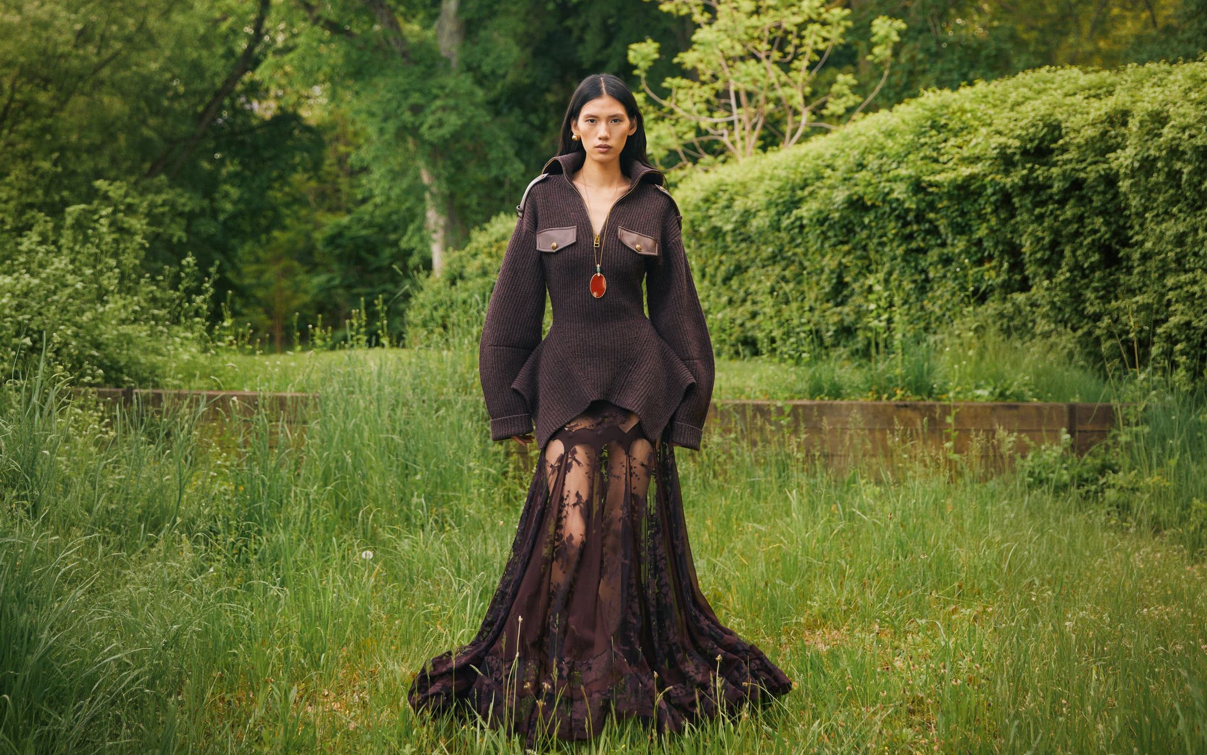 Woman wearing dark brown jacket with flowy gown.