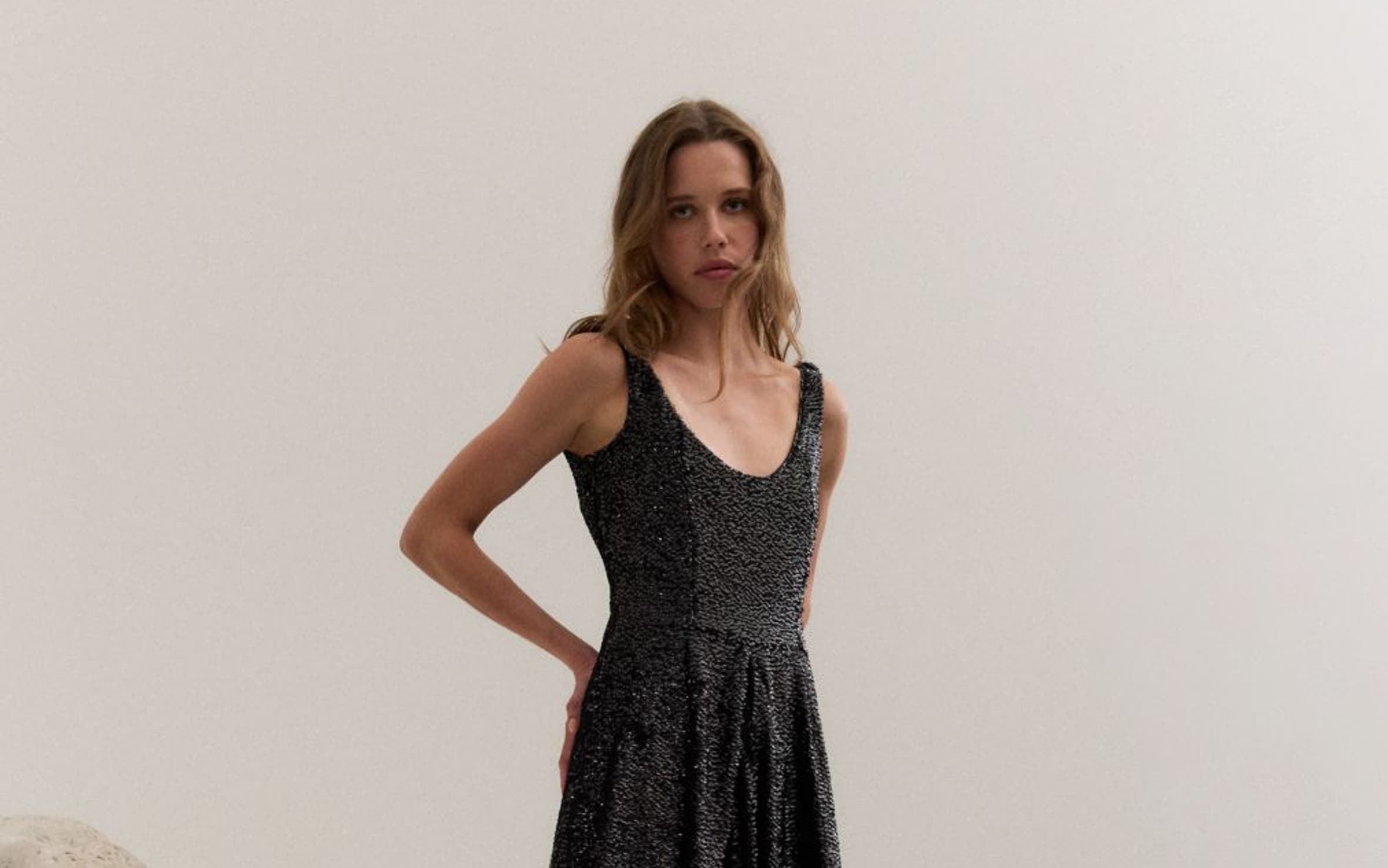 Woman wearing a sparkling party dress and heels next to a rock sculpture.