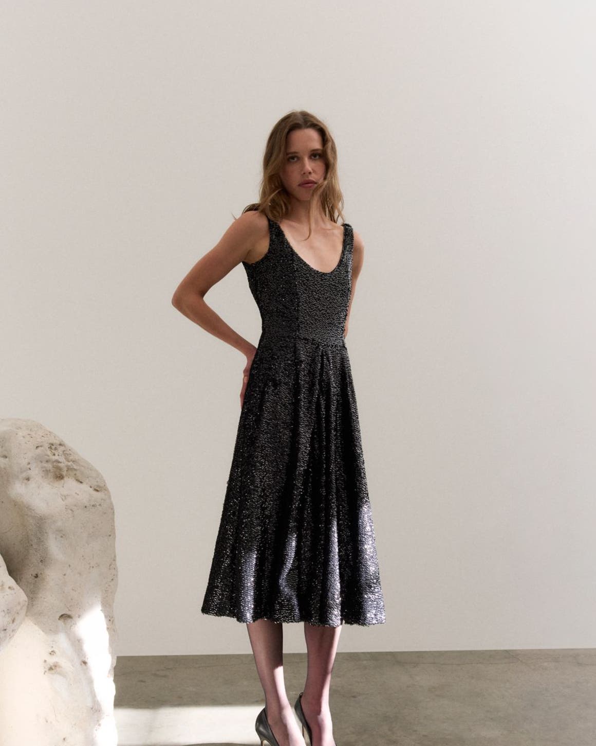 Woman wearing a sparkling party dress and heels next to a rock sculpture.