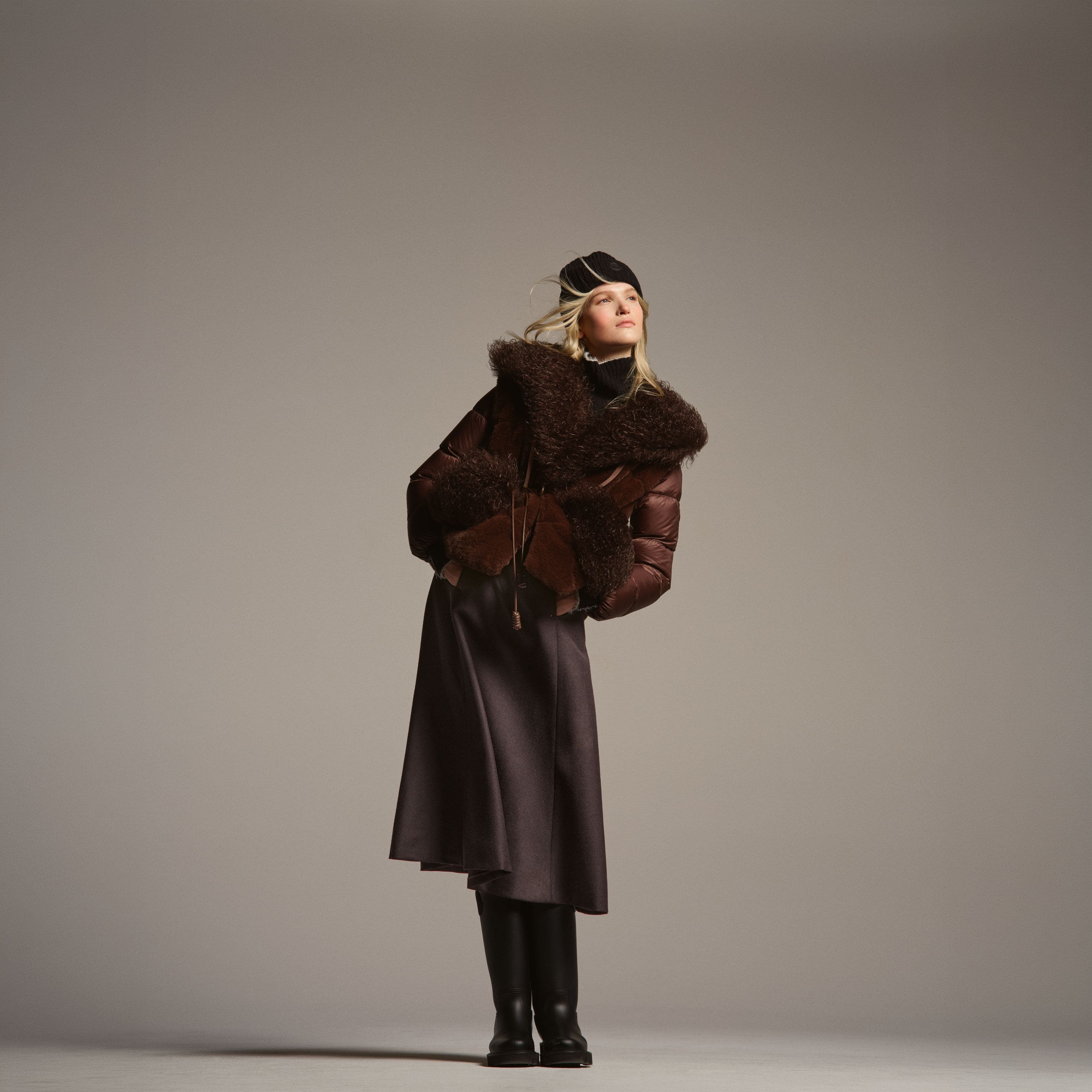 A woman wearing a puffer, skirt, and boots.