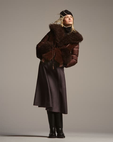 A woman wearing a puffer, skirt, and boots.