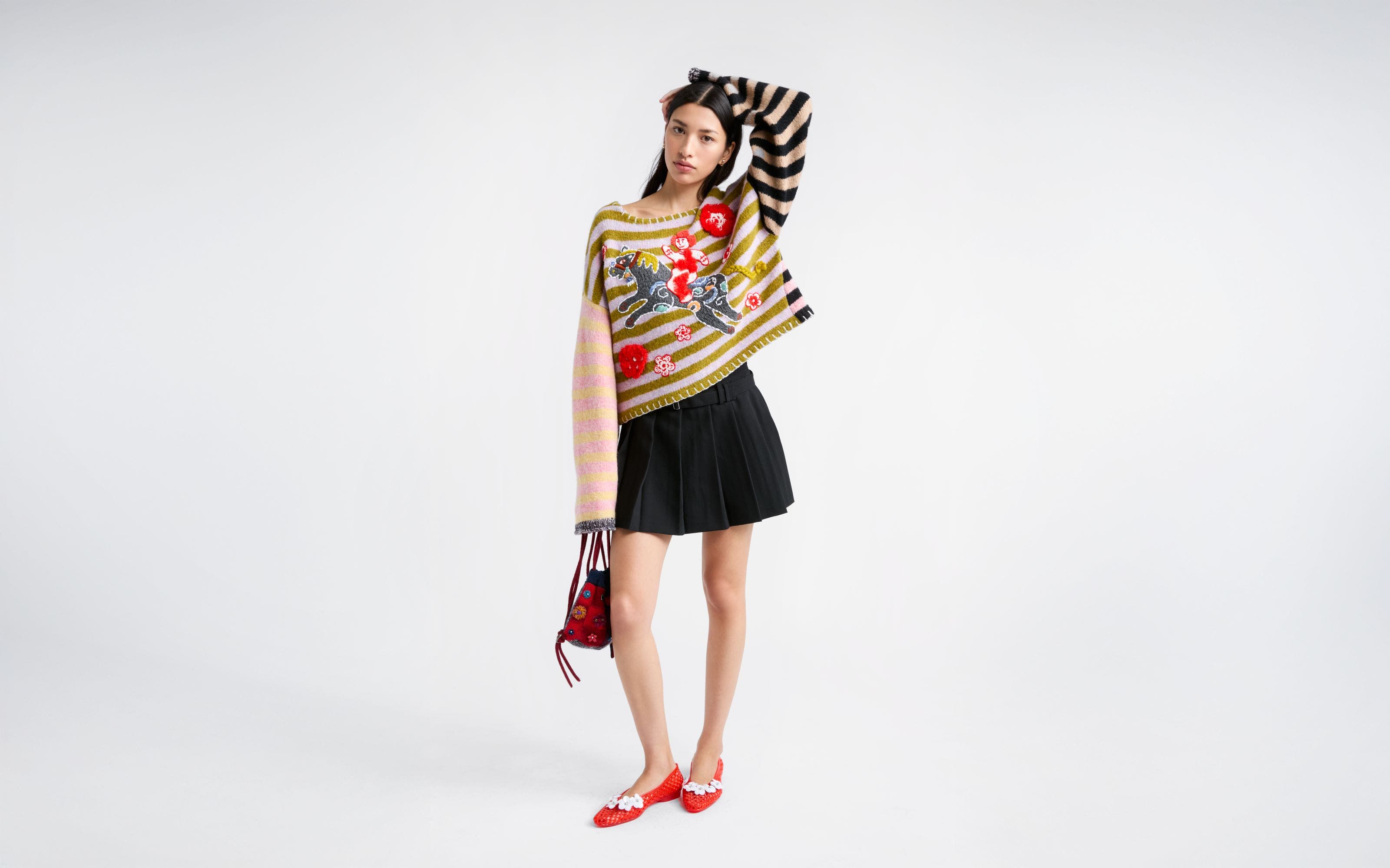 Woman wearing a sweater, pleated skirt, ballet flats and a handbag.