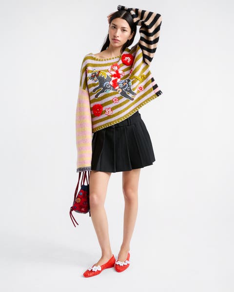 Woman wearing a sweater, pleated skirt, ballet flats and a handbag.