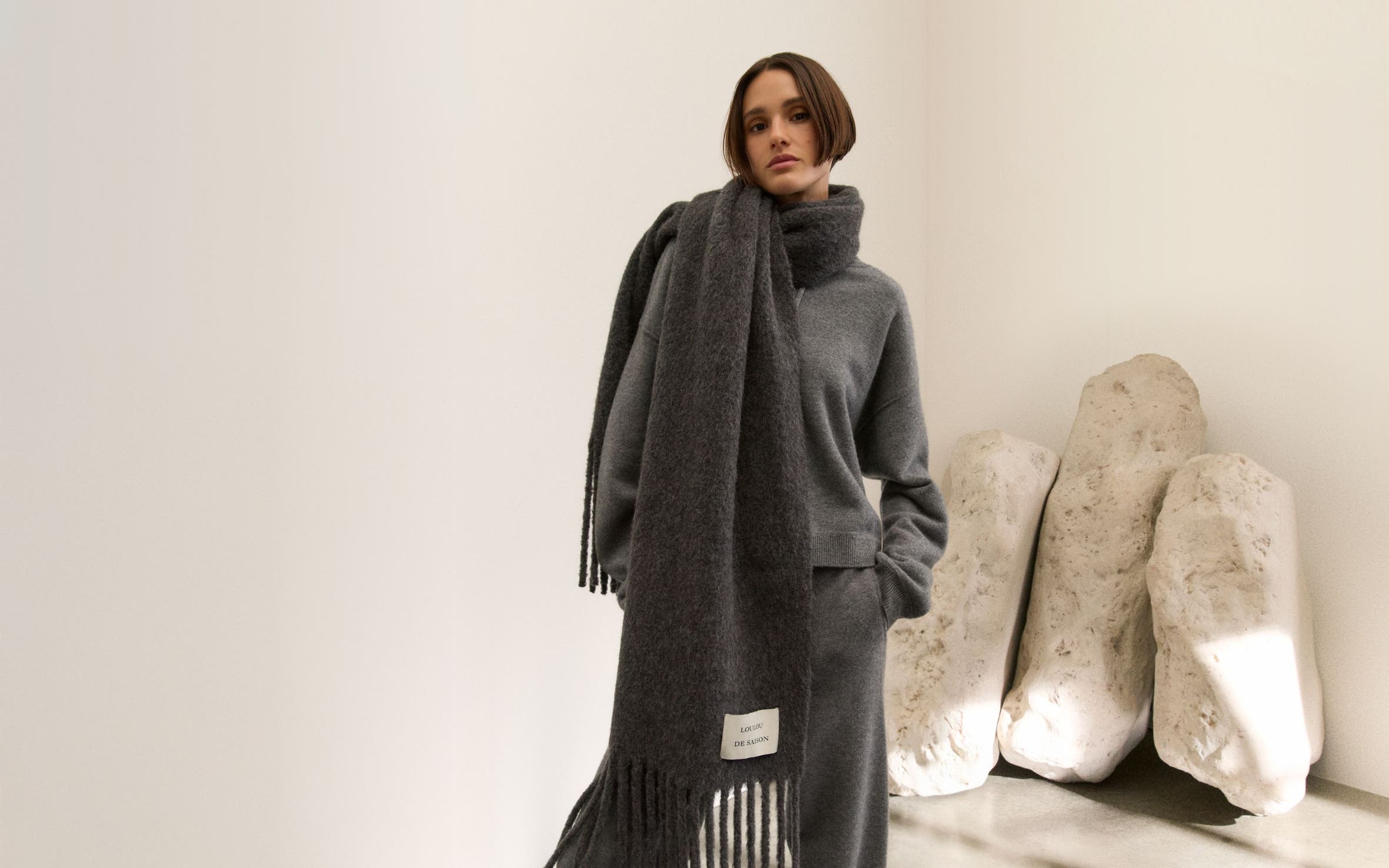 Woman wearing a grey knit hoodie, pants and oversized scarf.