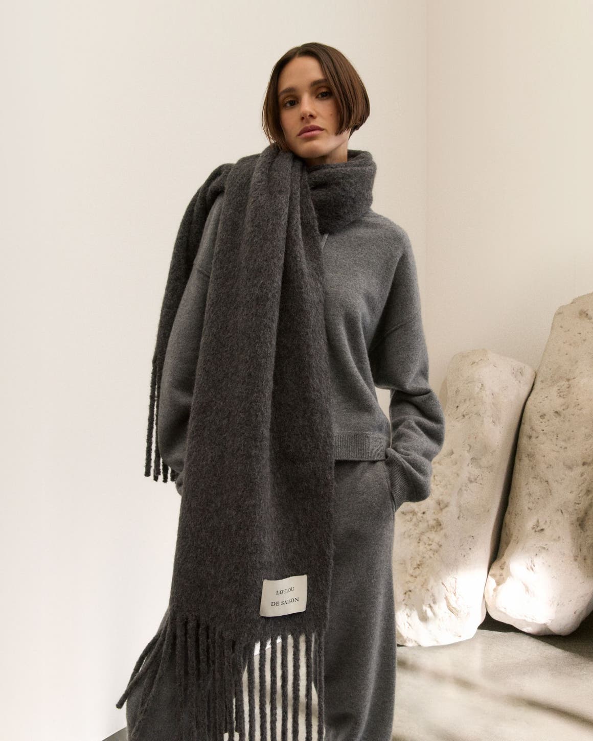 Woman wearing a grey knit hoodie, pants and oversized scarf.