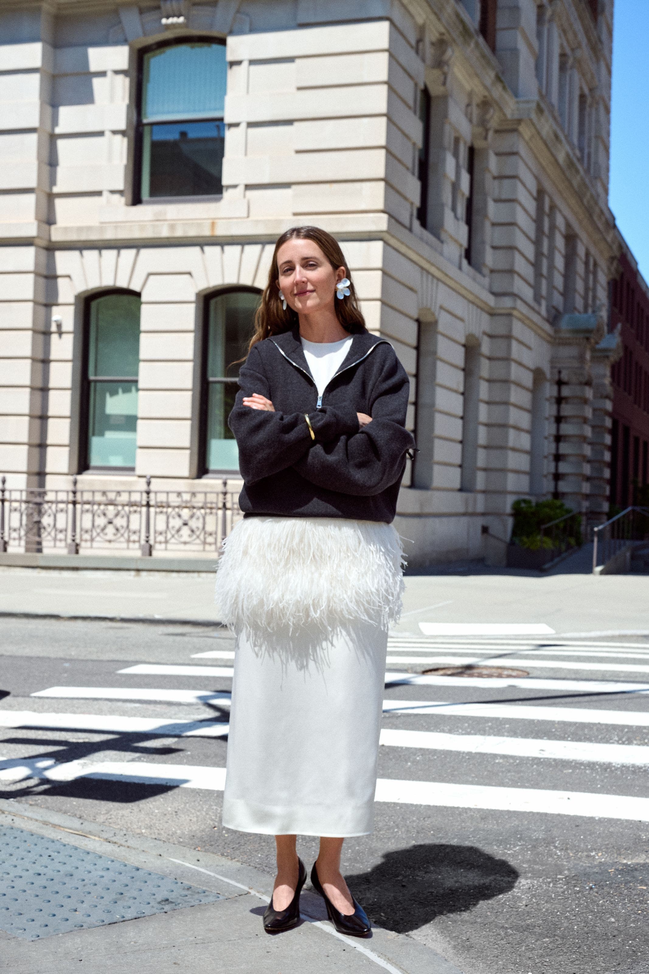 Woman in a black jacket and white dress standing on a city street.