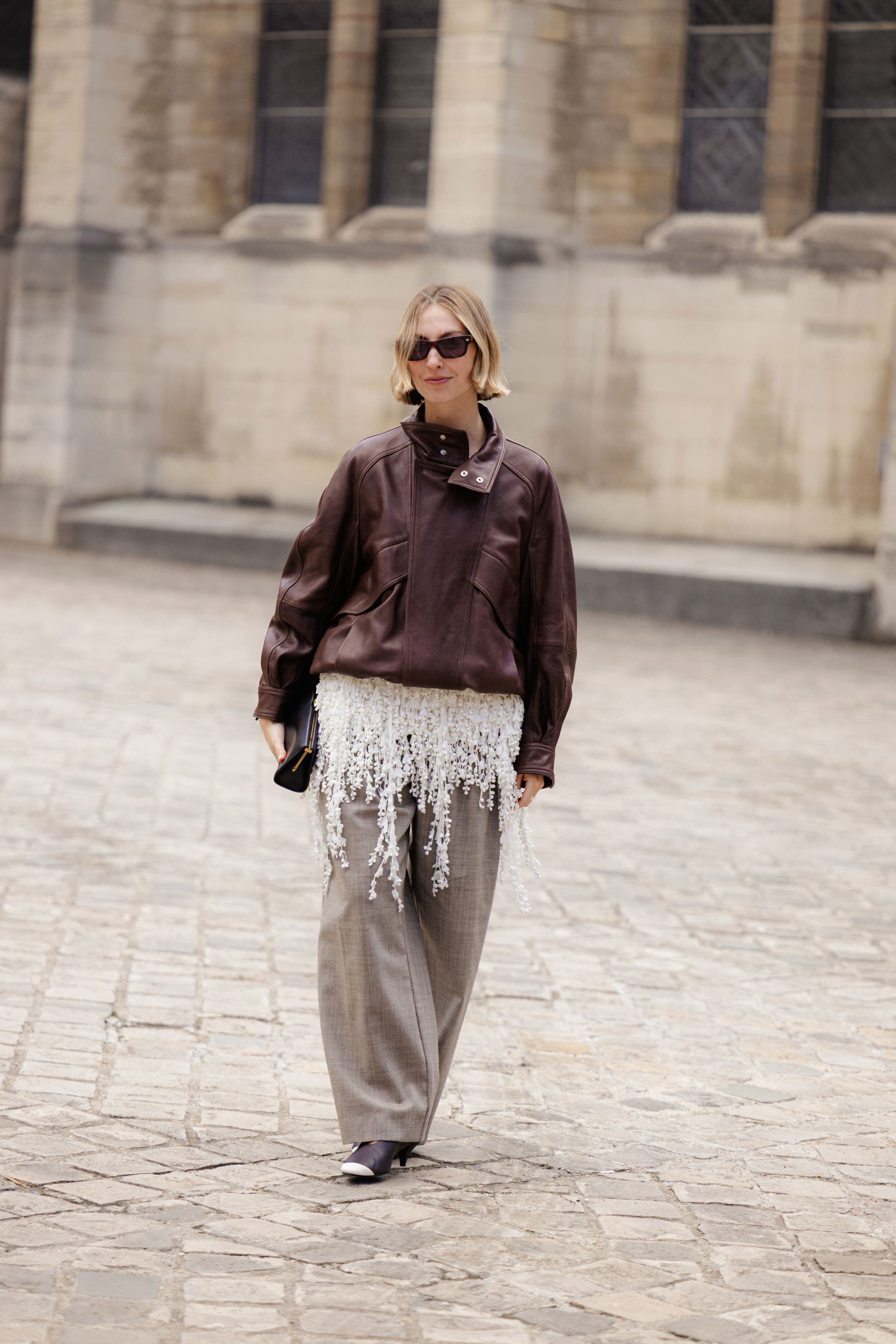Woman in a brown leather jacket and light-brown pants.