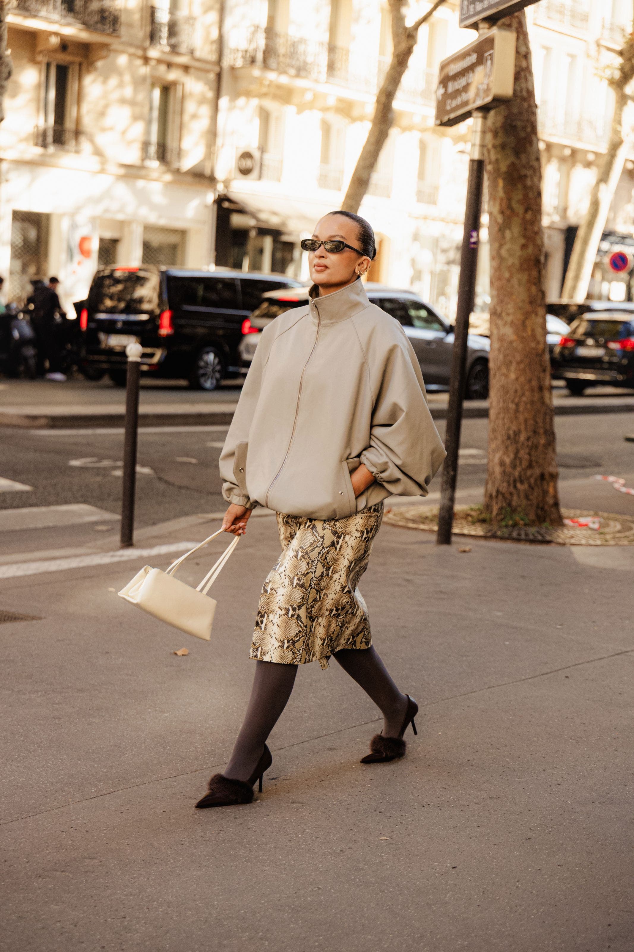 A woman wearing a tan jacket, snake-print skirt and heels.