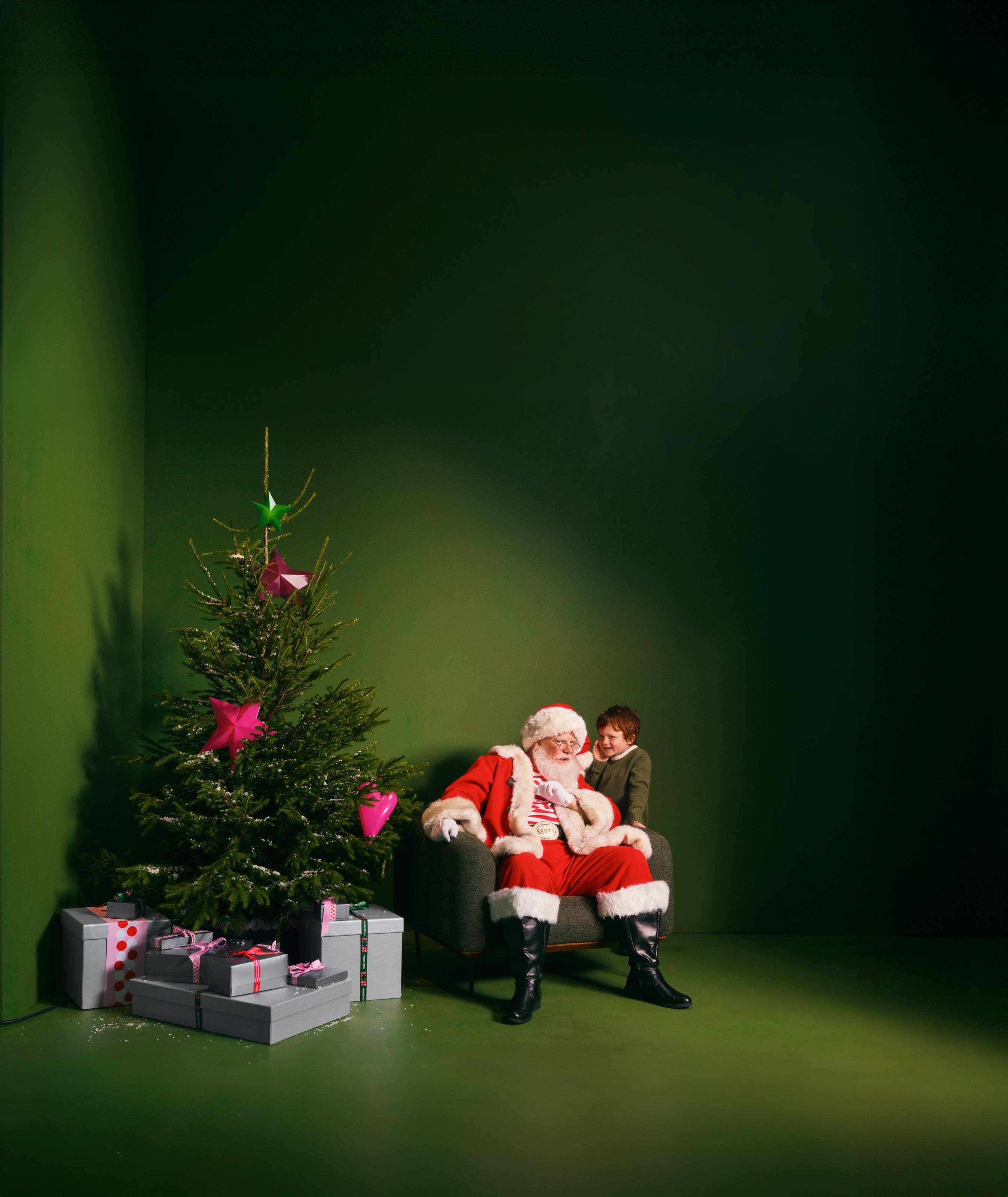 A boy whispering into Santa's ear.