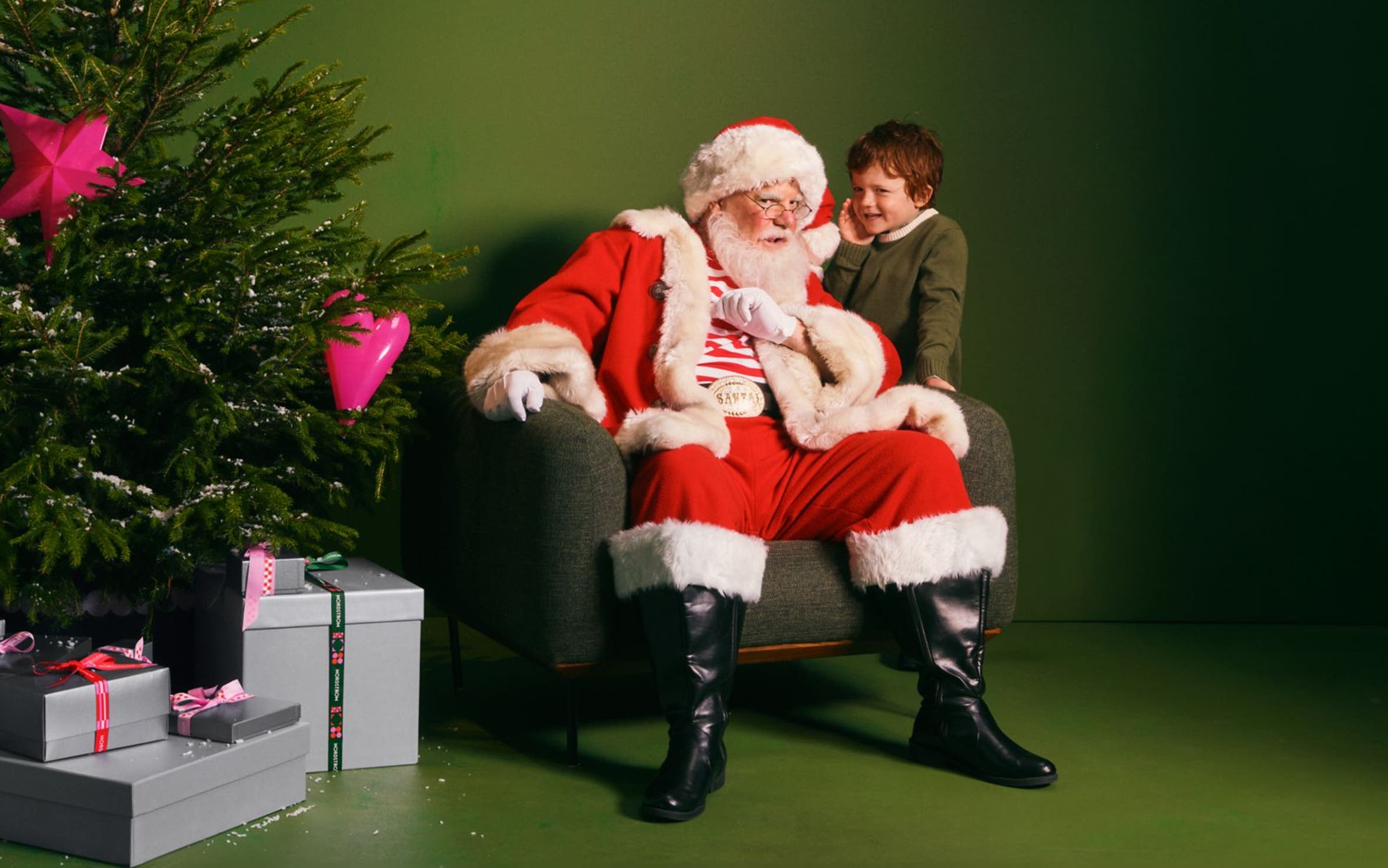 A boy whispering into Santa's ear.