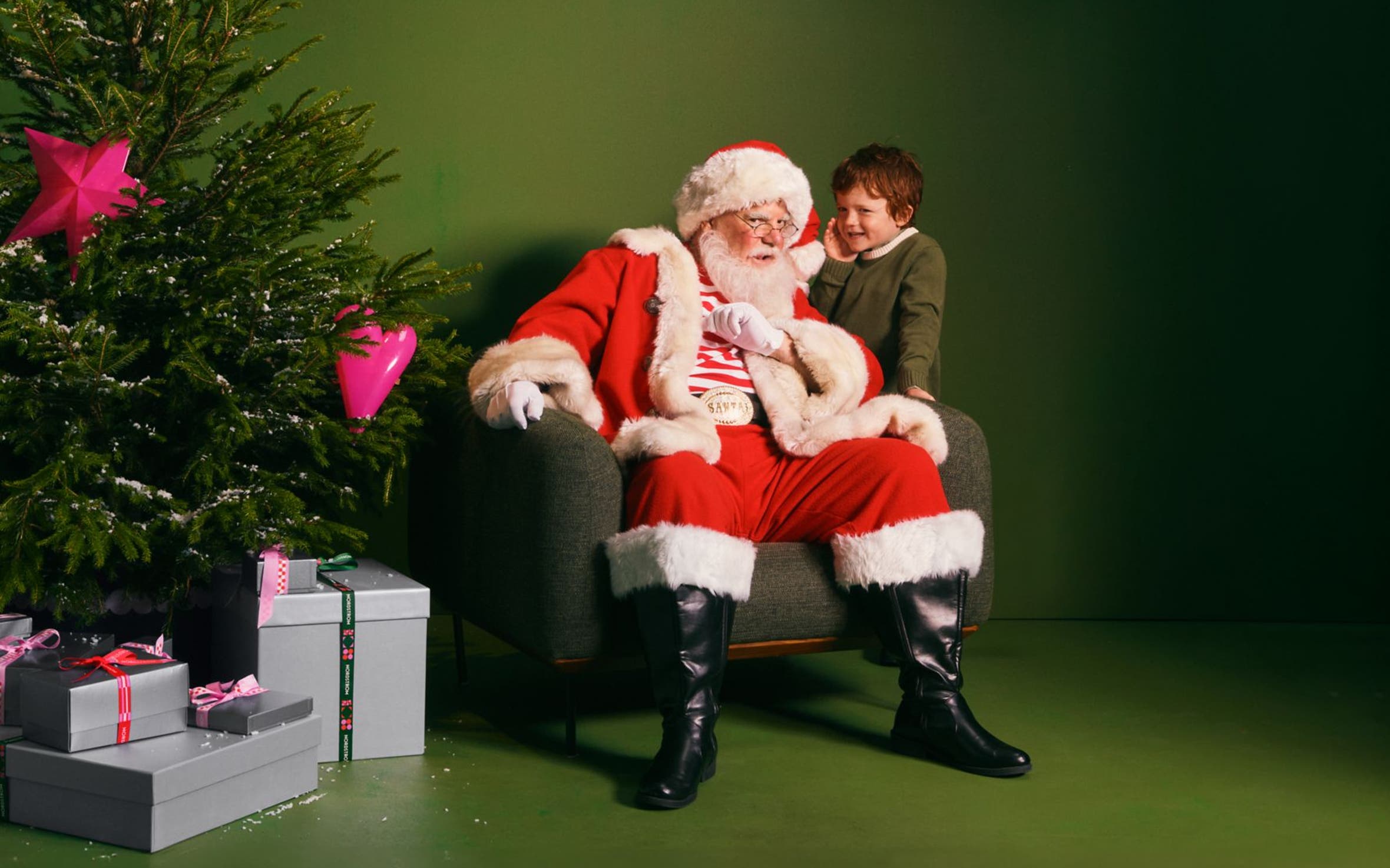 A boy whispering into Santa's ear.