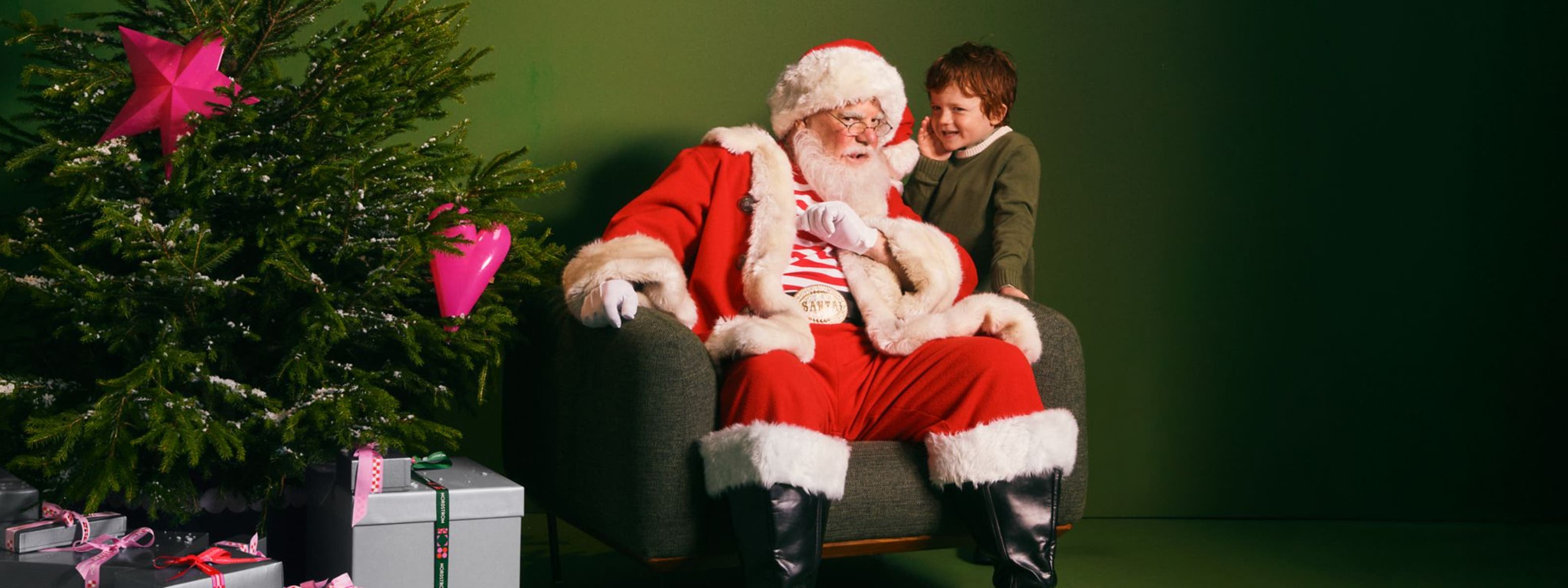 A boy whispering into Santa's ear.
