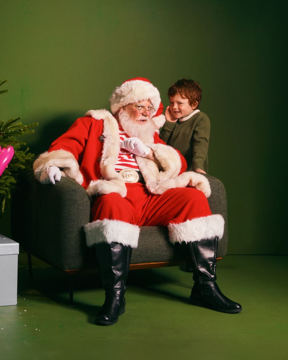 A boy whispering into Santa's ear.