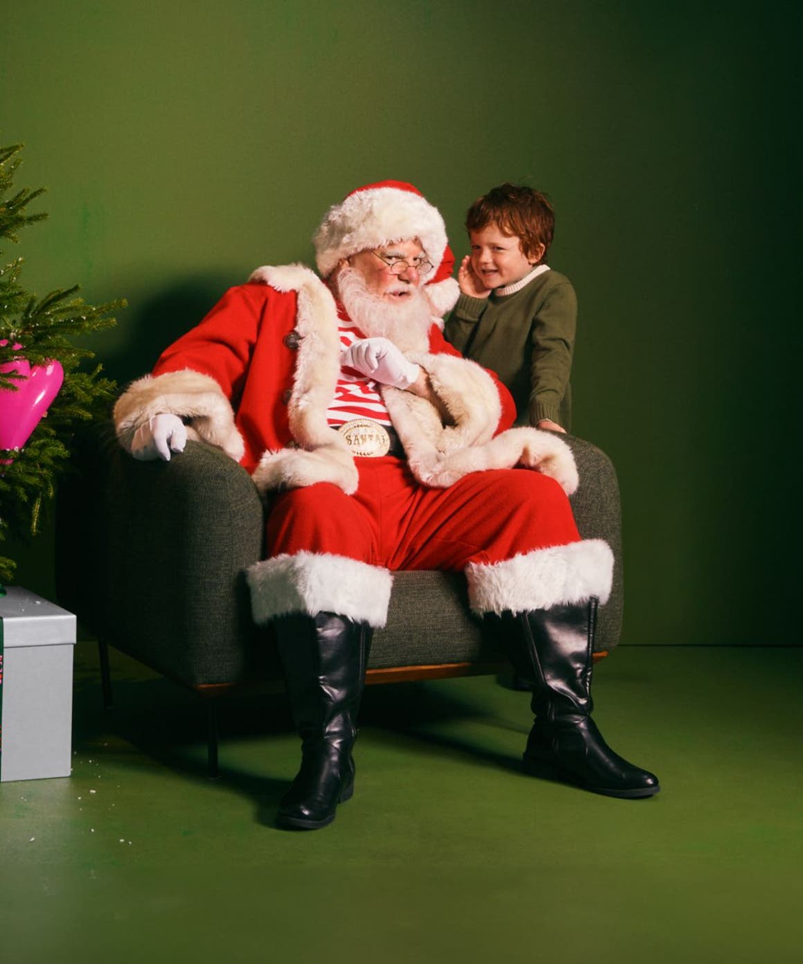 A boy whispering into Santa's ear.