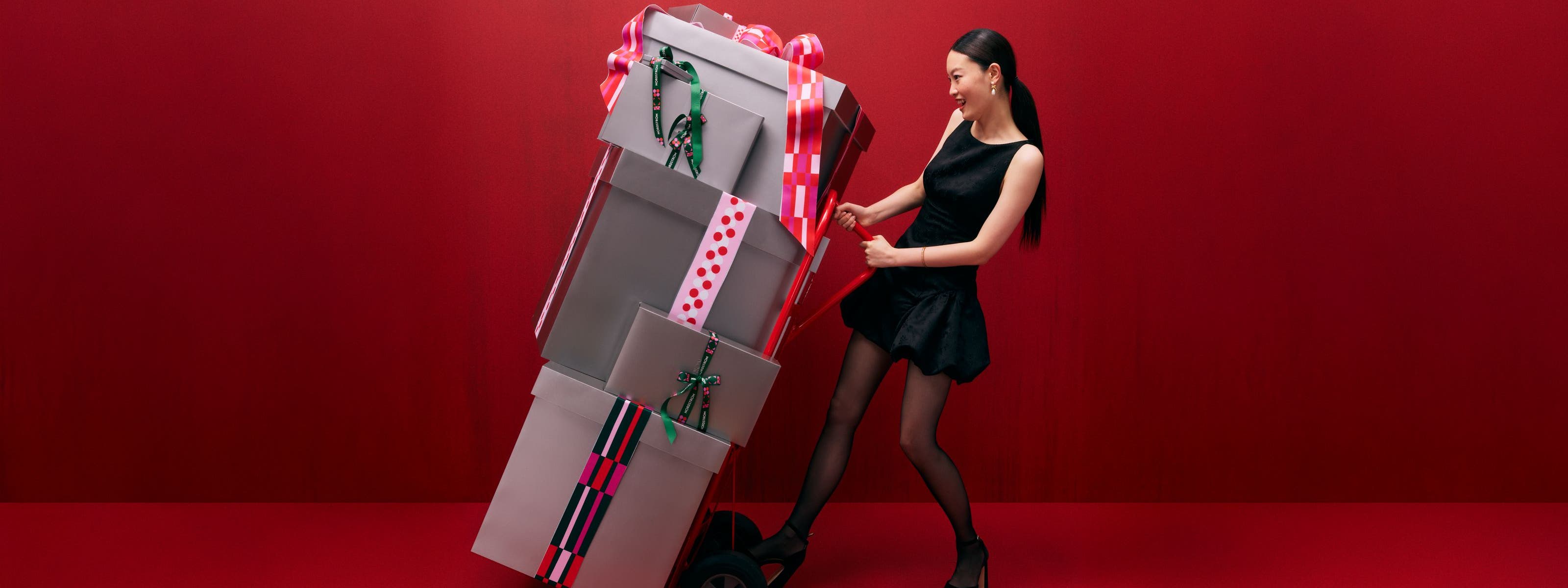 A woman pushing a hand truck loaded with gift boxes.