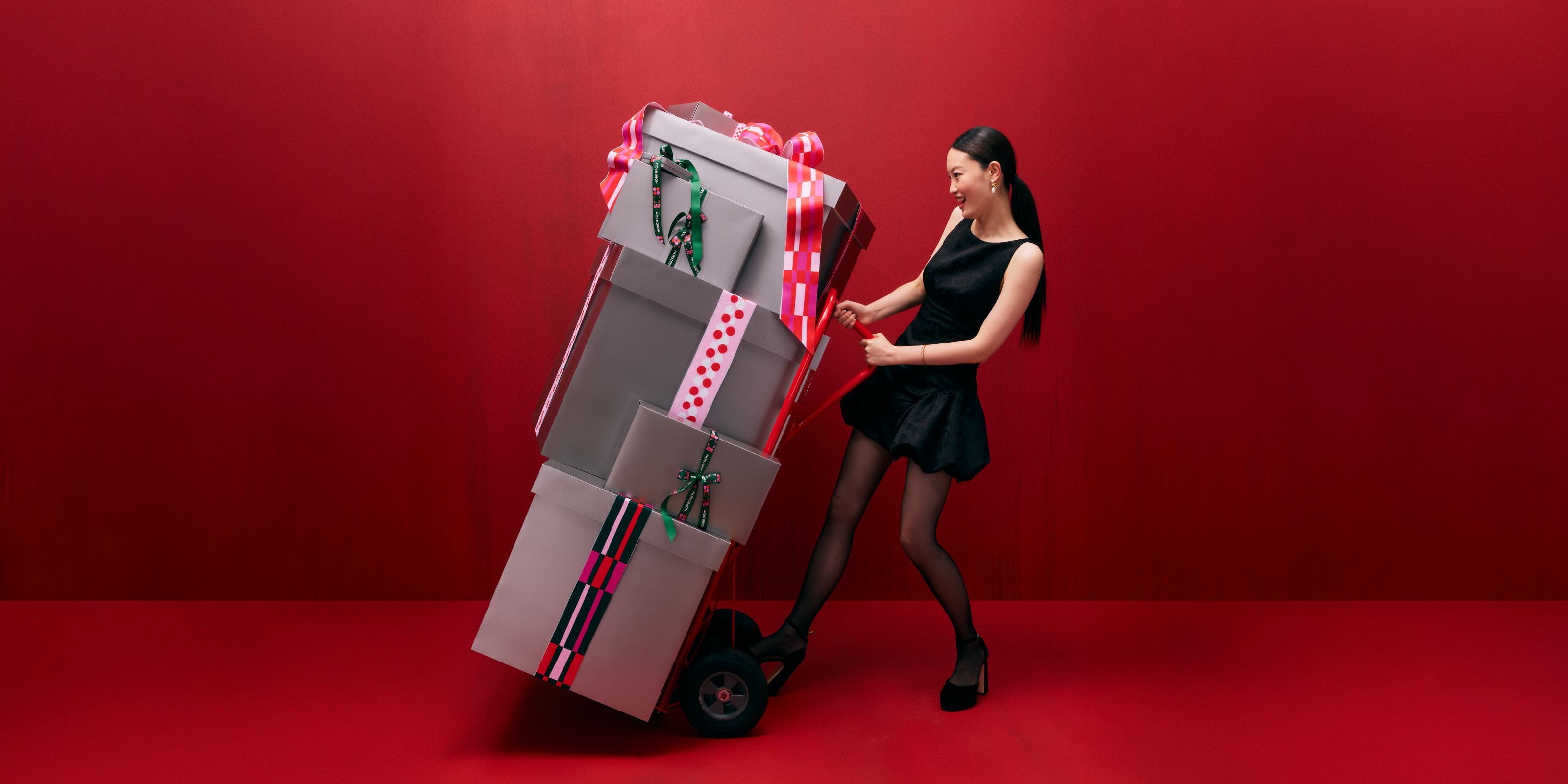 A woman pushing a hand truck loaded with gift boxes.