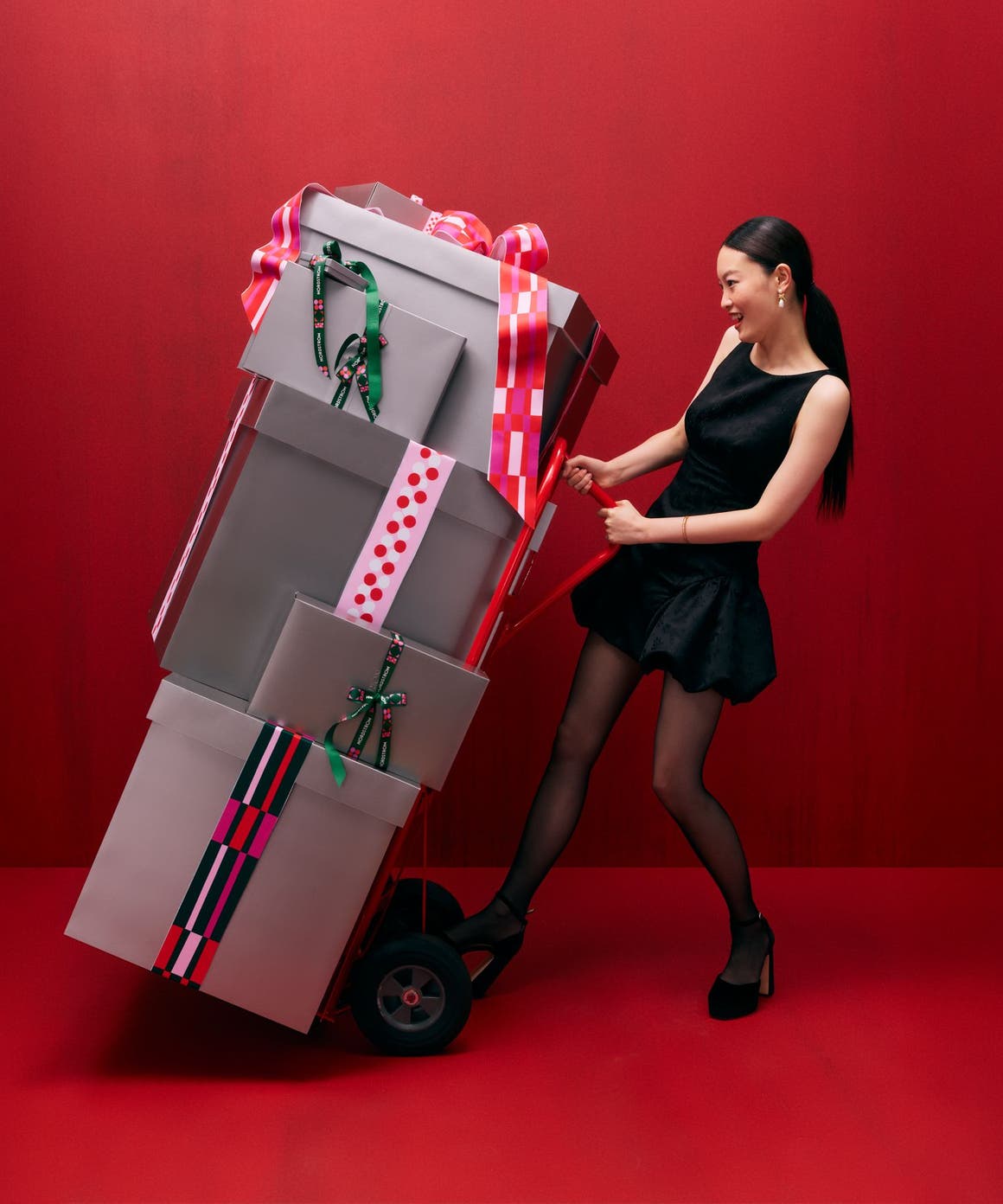 A woman pushing a hand truck loaded with gift boxes.