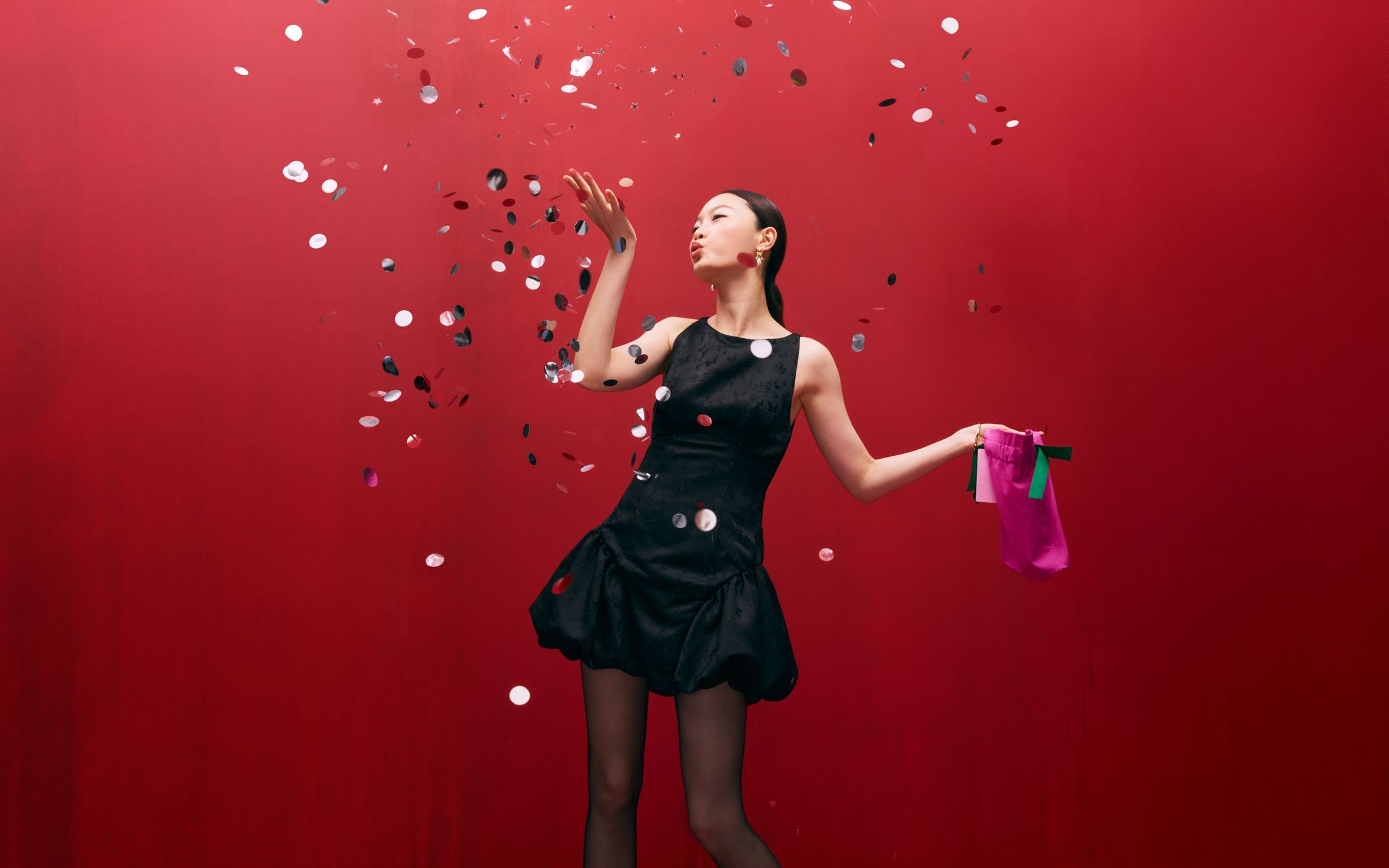 A woman wearing a cocktail dress and blowing confetti.