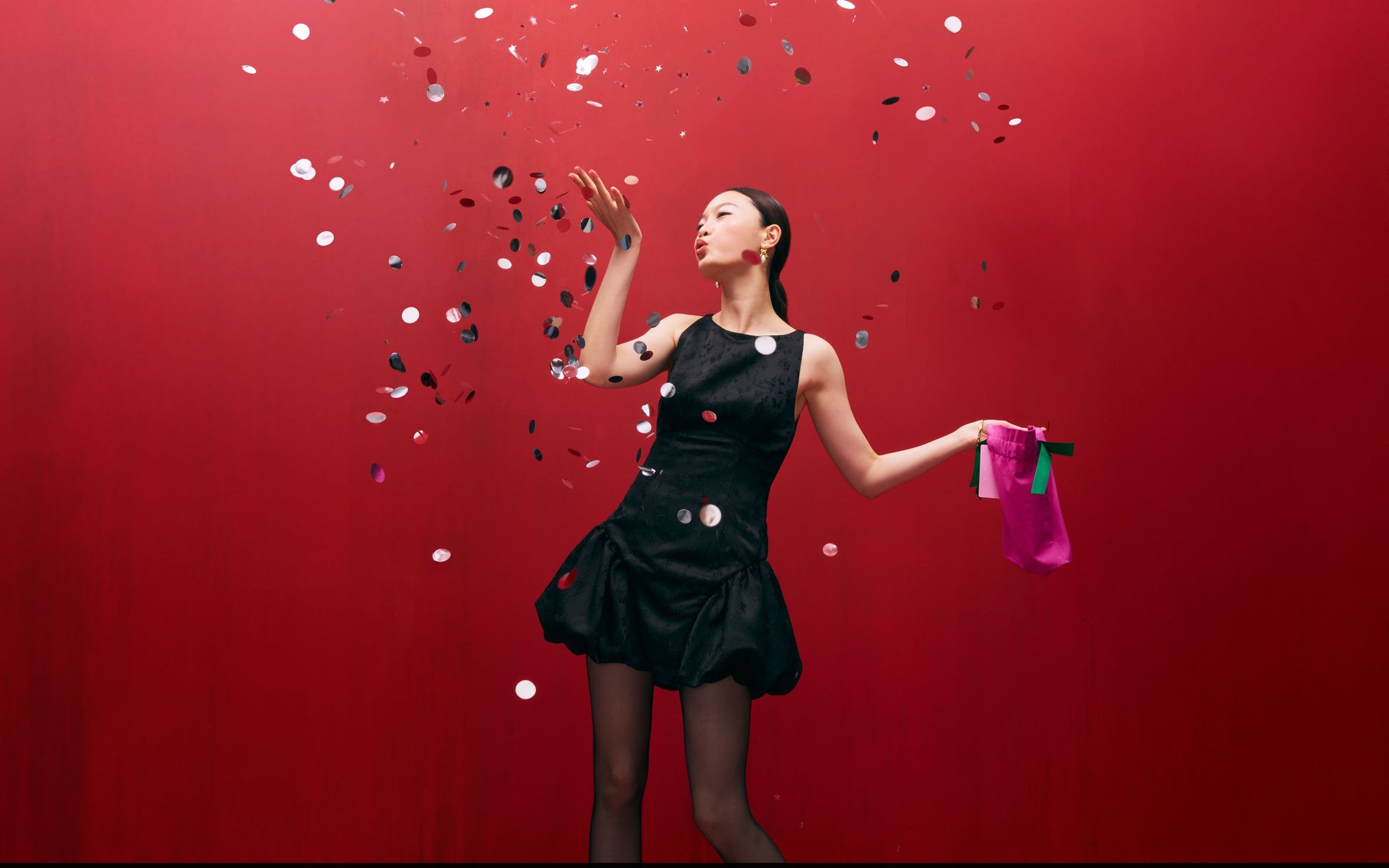 Woman wearing a cocktail dress and blowing confetti.