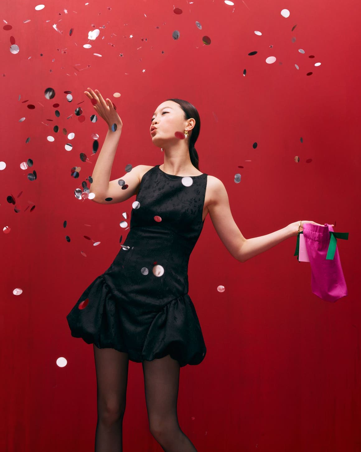 A woman wearing a cocktail dress and blowing confetti.