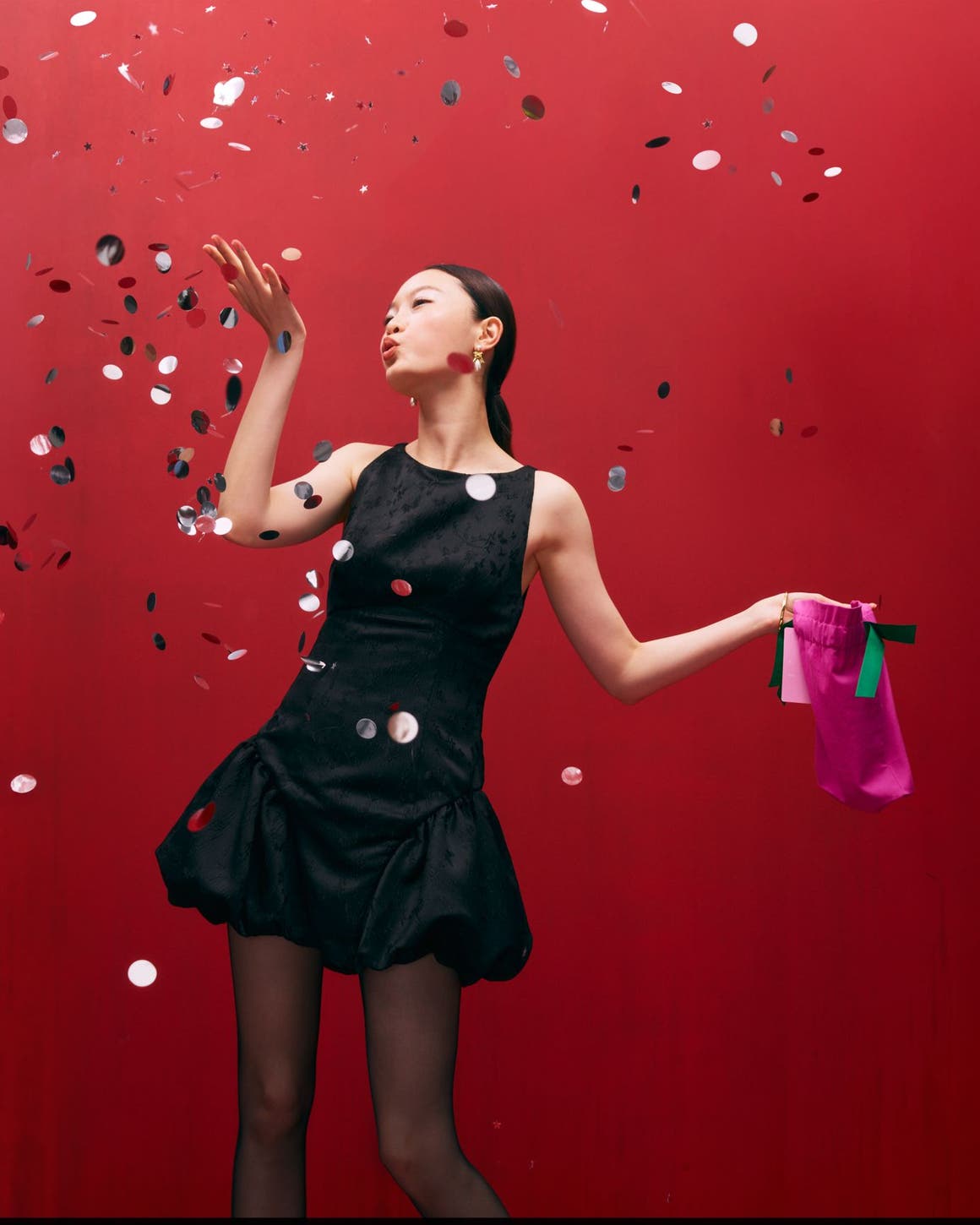 Woman wearing a cocktail dress and blowing confetti.