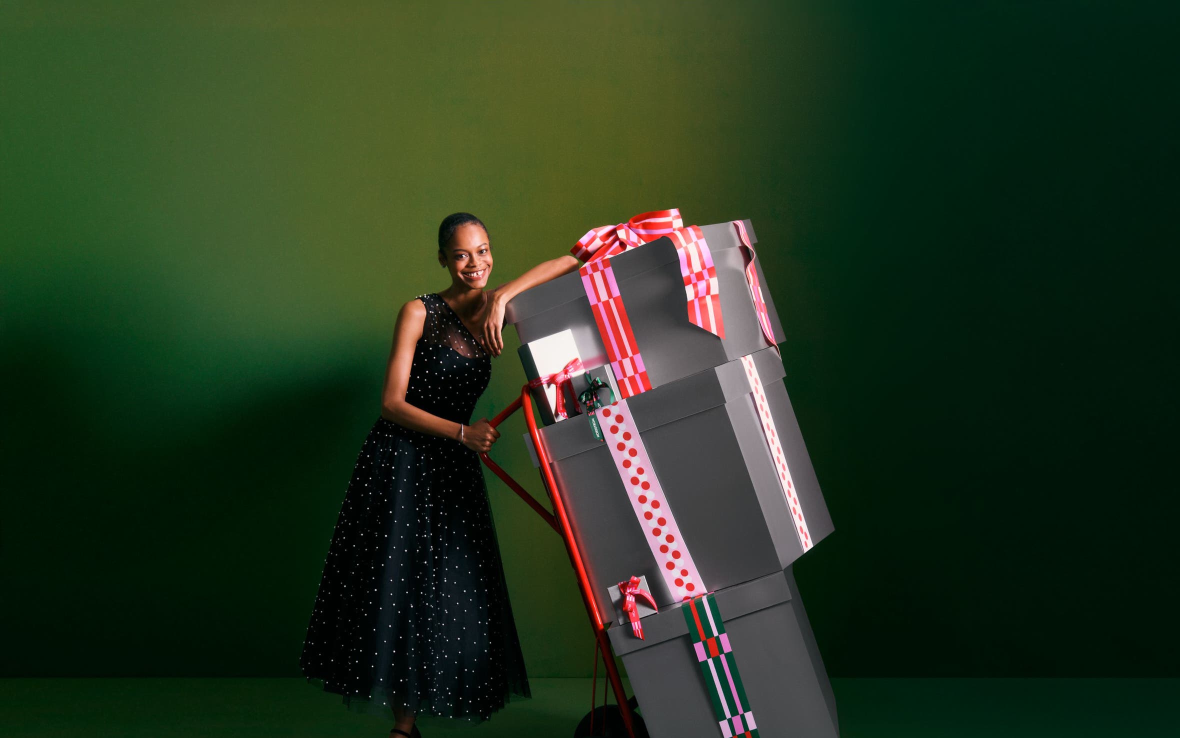 A woman with a stack of gift boxes on a dolly.