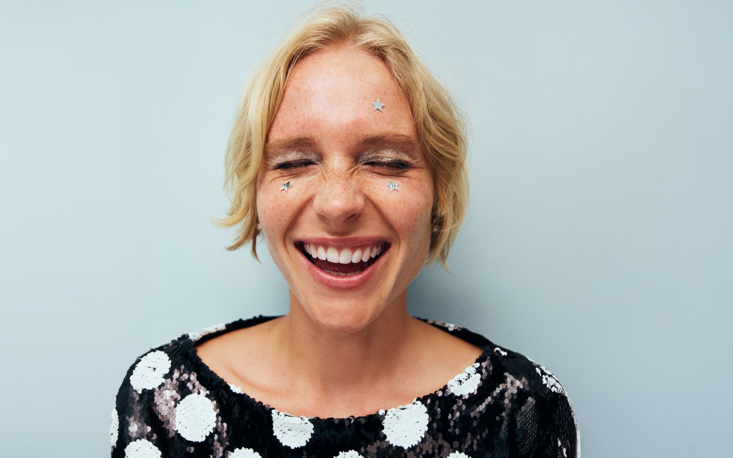 A woman with star stickers on her face laughing.