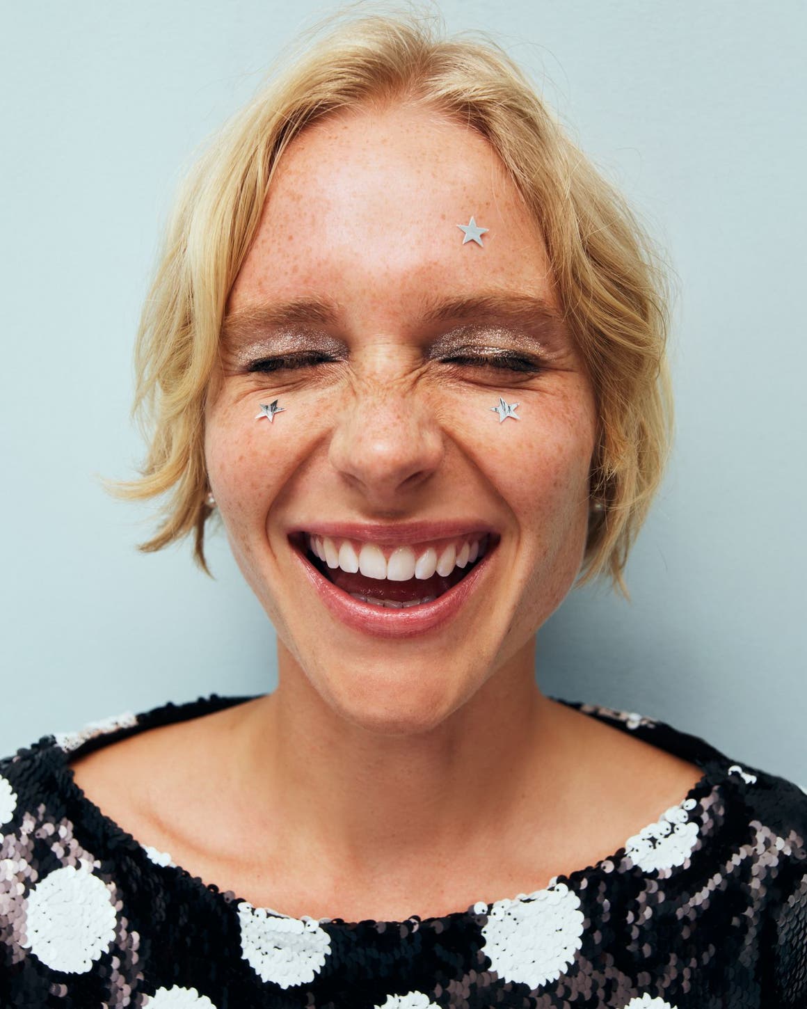 A woman with star stickers on her face laughing.