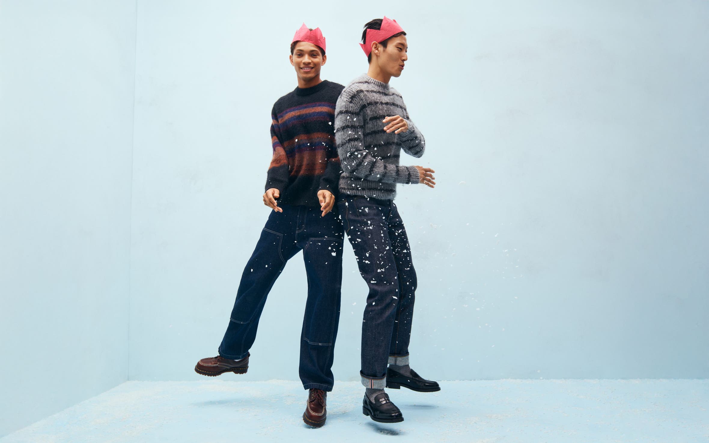 Two men wearing paper crowns, sweaters and jeans.