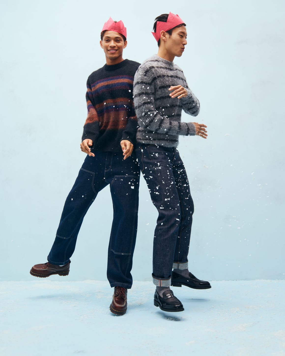 Two men wearing paper crowns, sweaters and jeans.