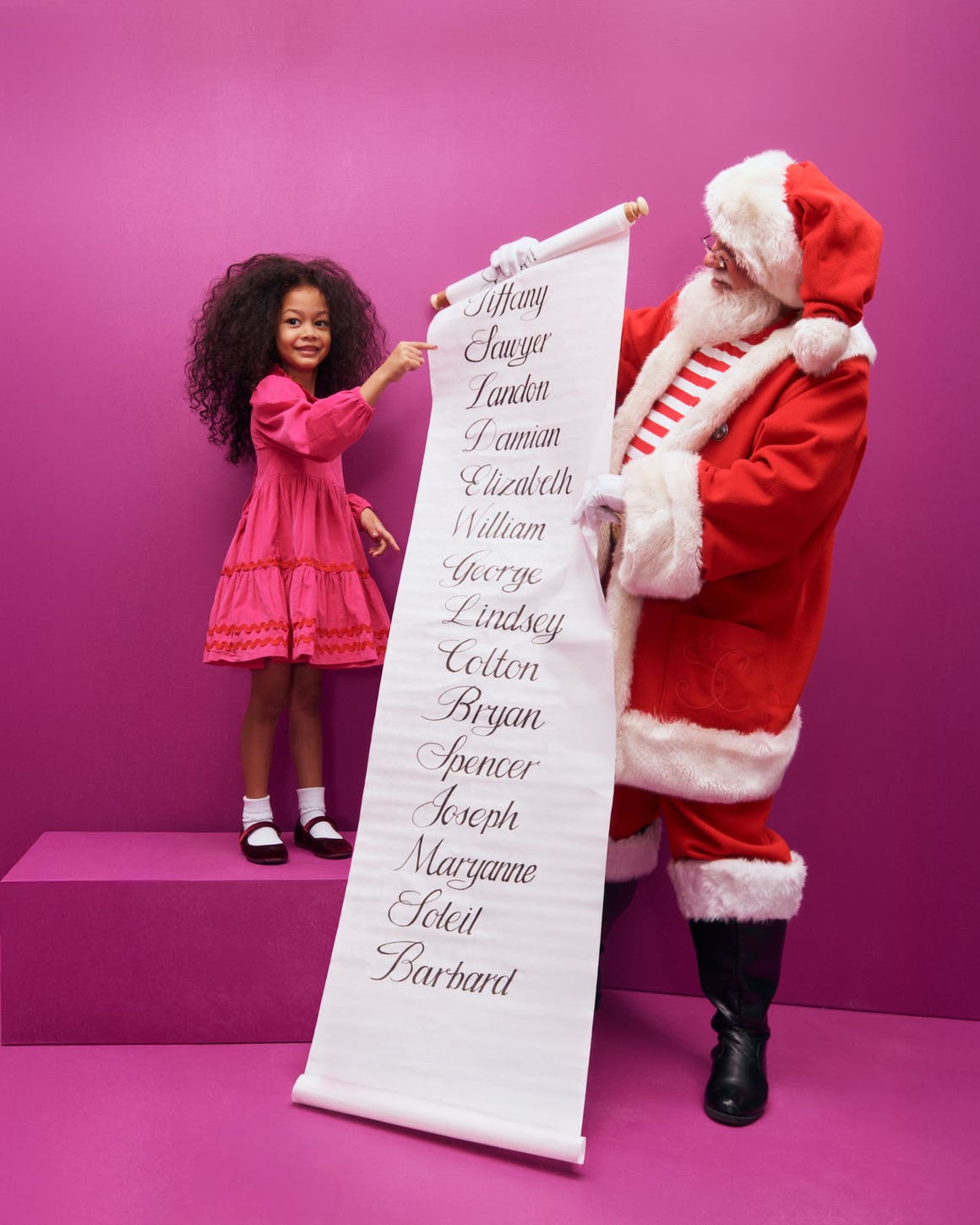 A little girl and Santa looking at a list of names.