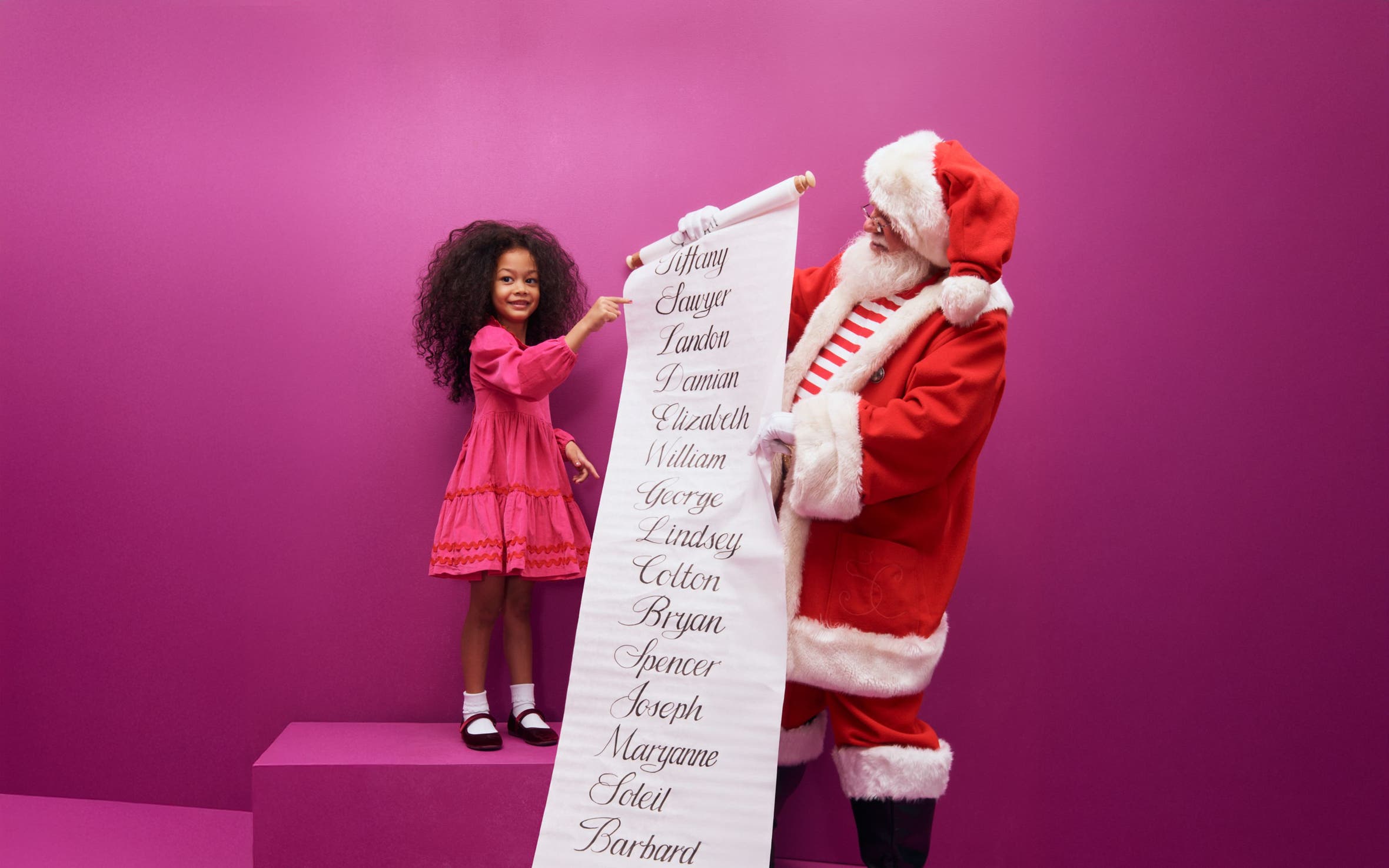 A little girl and Santa looking at a list of names.