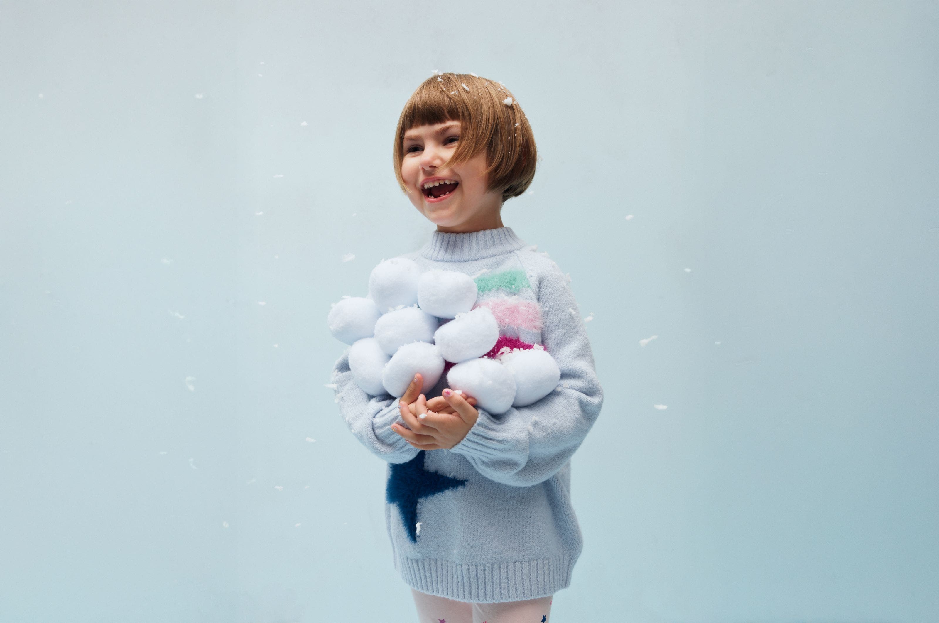 A girl holding a pile of snowballs.