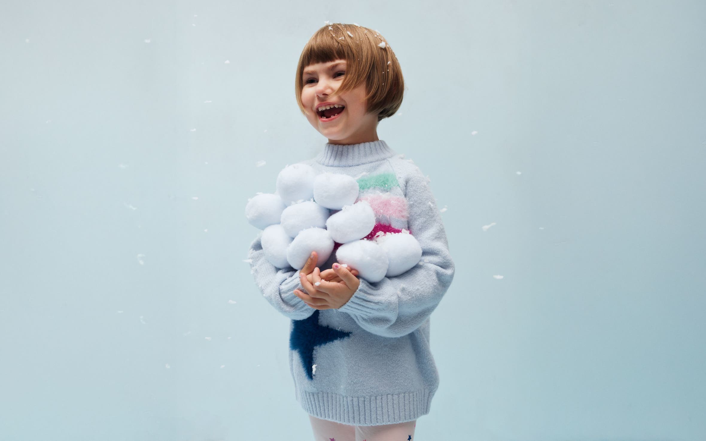 A girl holding a pile of snowballs.