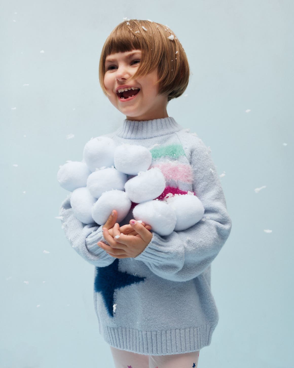 A girl holding a pile of snowballs.