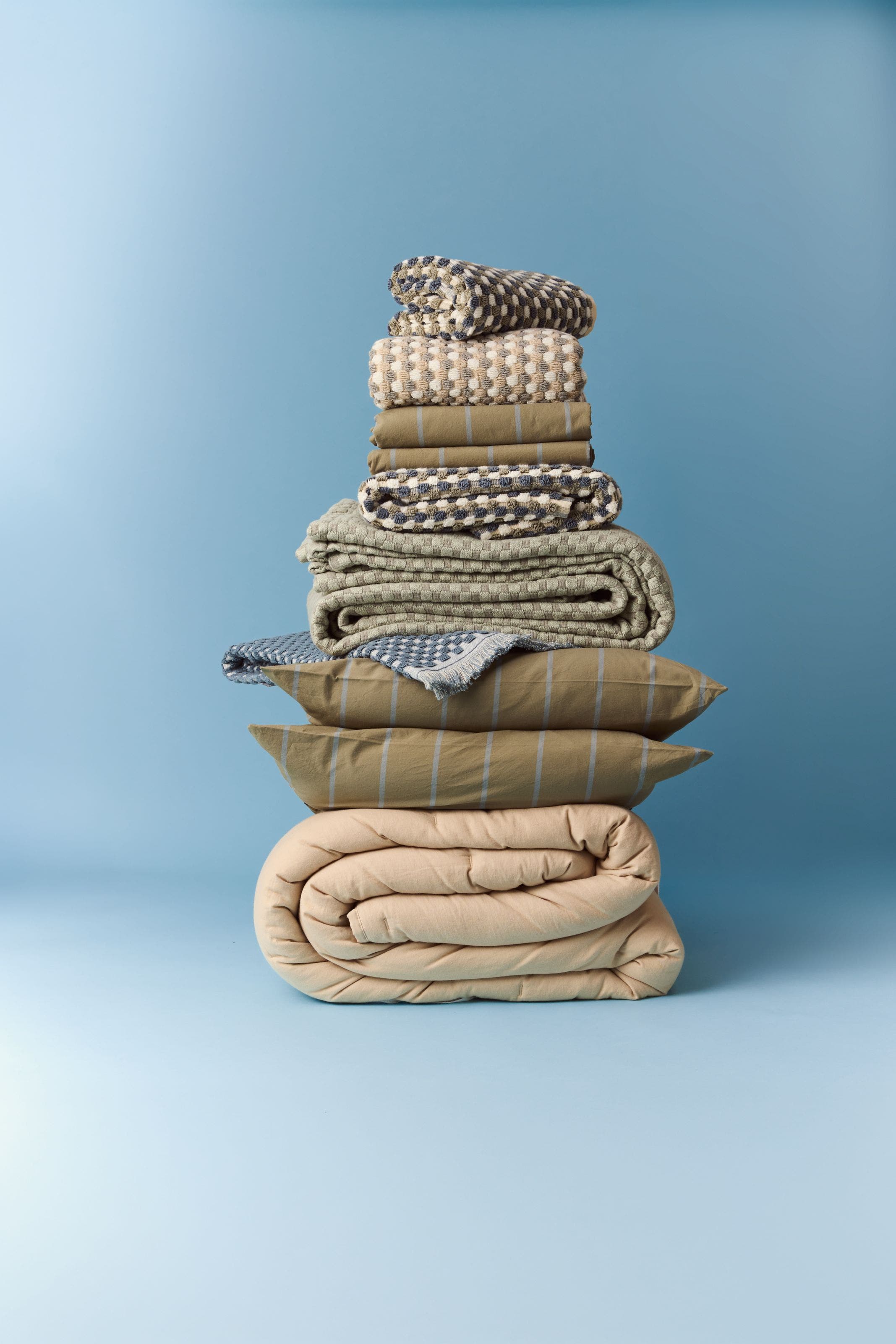 A stack of bed linens in neutral colors. 