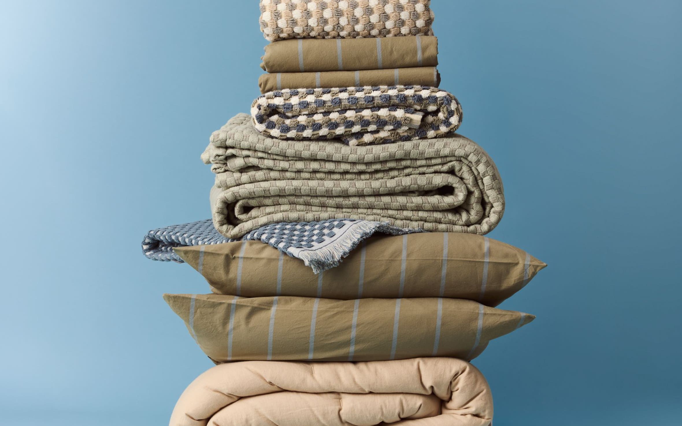 A stack of bed linens in neutral colors.