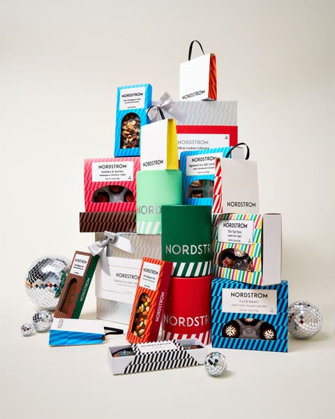 Stacked tower of Nordstrom-branded holiday gift boxes and bags filled with chocolates, cookies, and sweets, surrounded by silver disco balls.