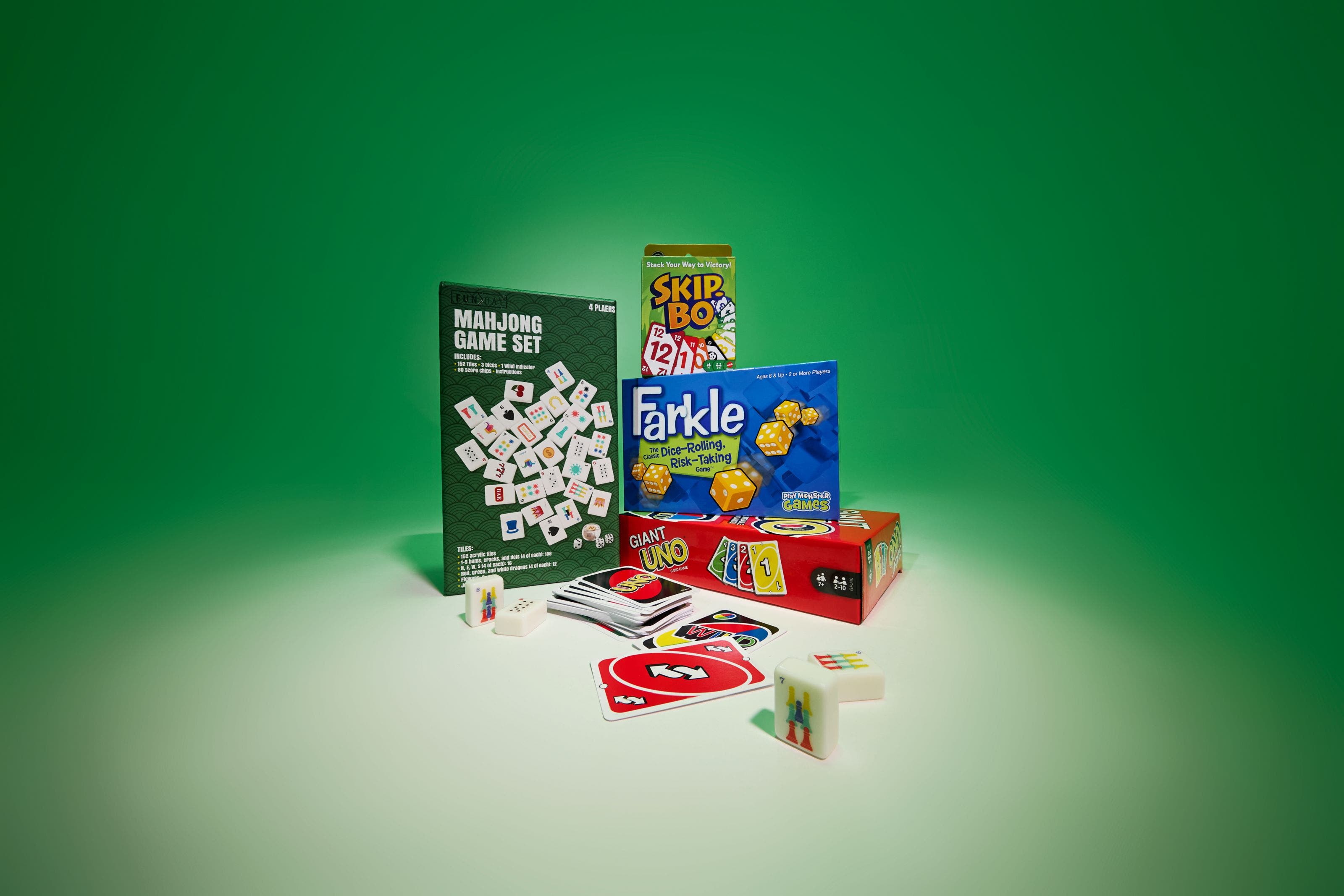 Mahjong set, Skip-Bo, Farkle, and games with loose tiles and cards on green.