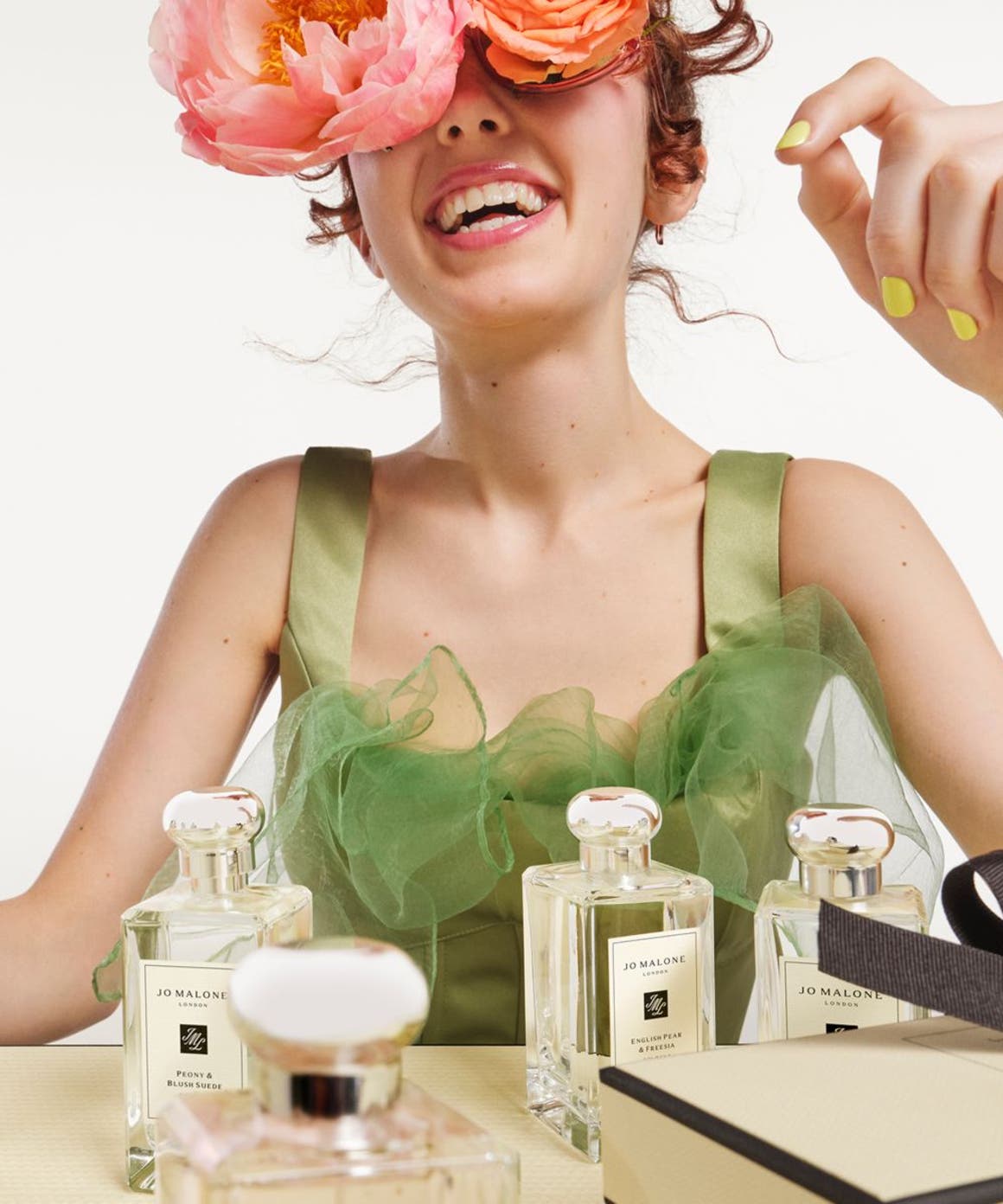 Woman with roses over her eyes with Jo Malone fragrances in front of her.