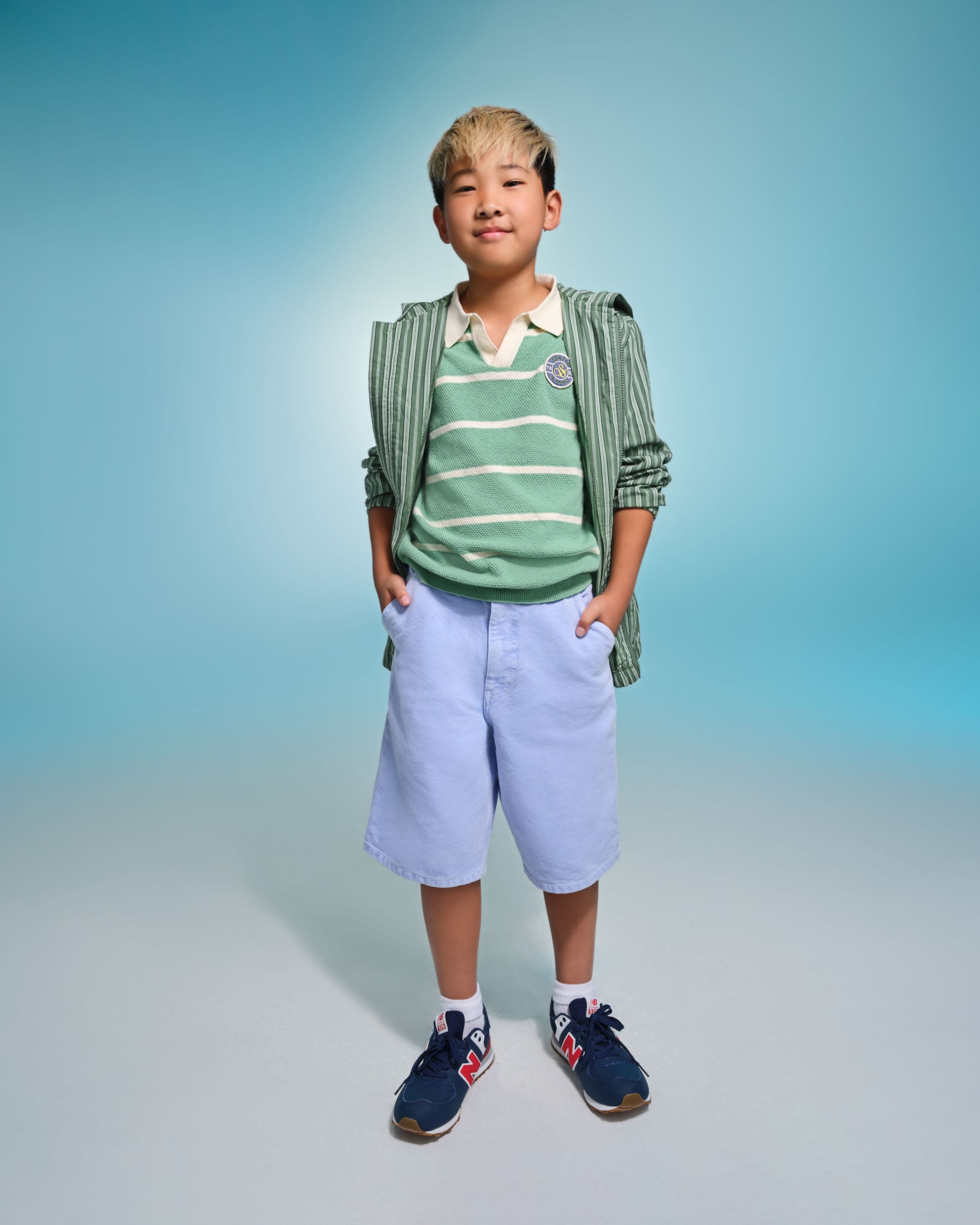 A child wearing a green and white stripped shirt with shorts and sneakers. 