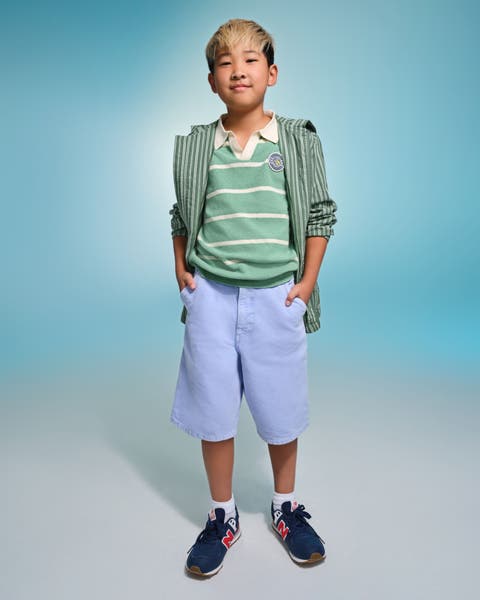 A child wearing a green and white stripped shirt with shorts and sneakers.