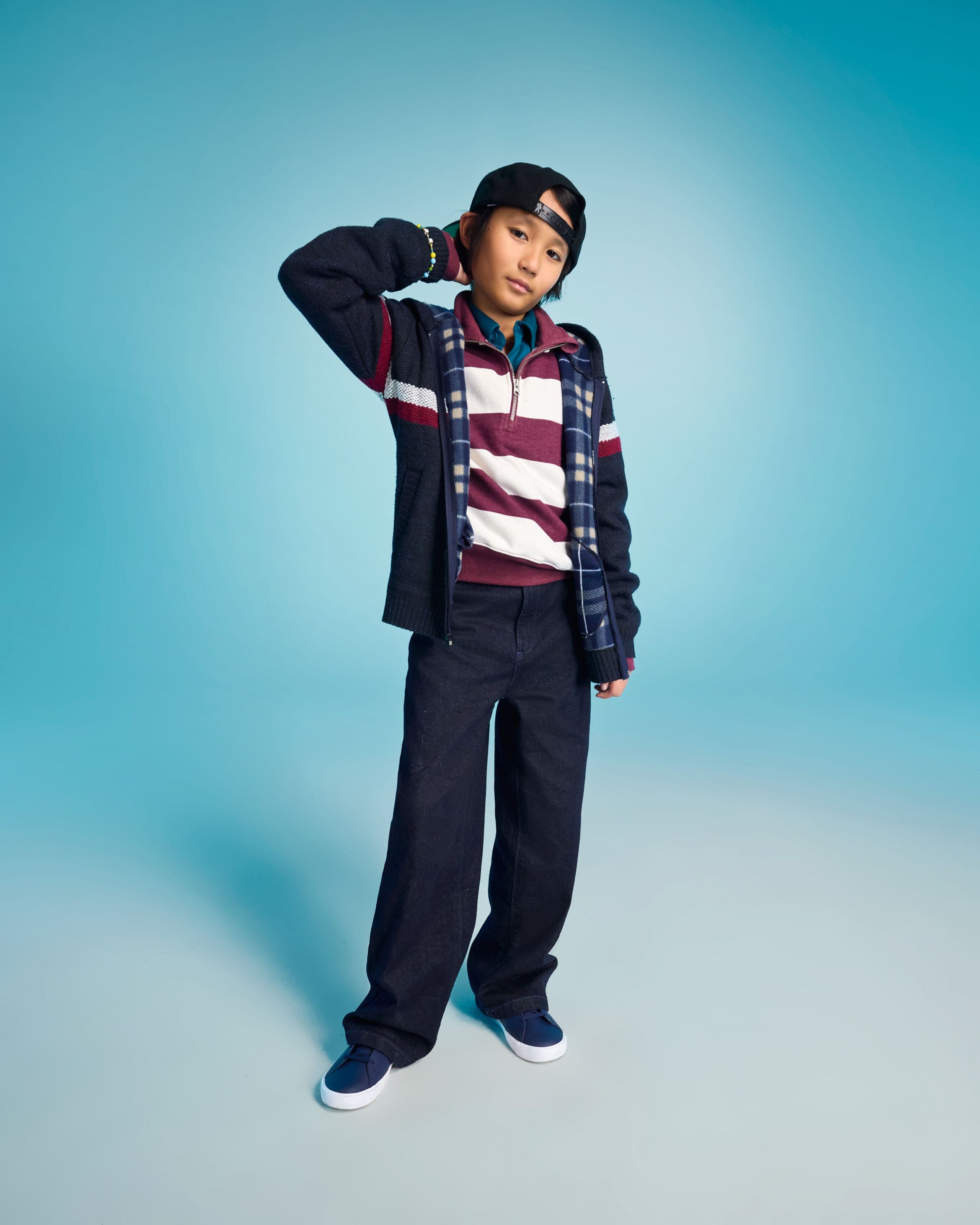 A child wearing a layered rugby stripe polo, plaid shirt, and navy wide-leg pants.